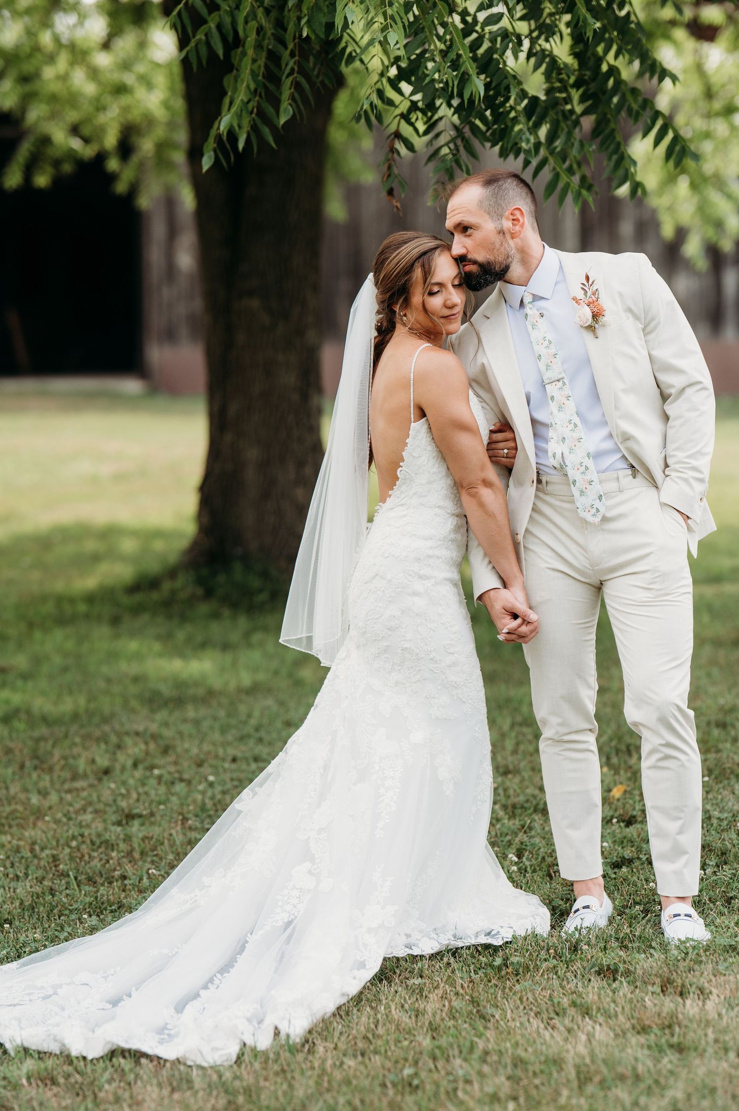 A series of wedding photos capturing the couple in white attire embracing on a grassy lawn under trees.