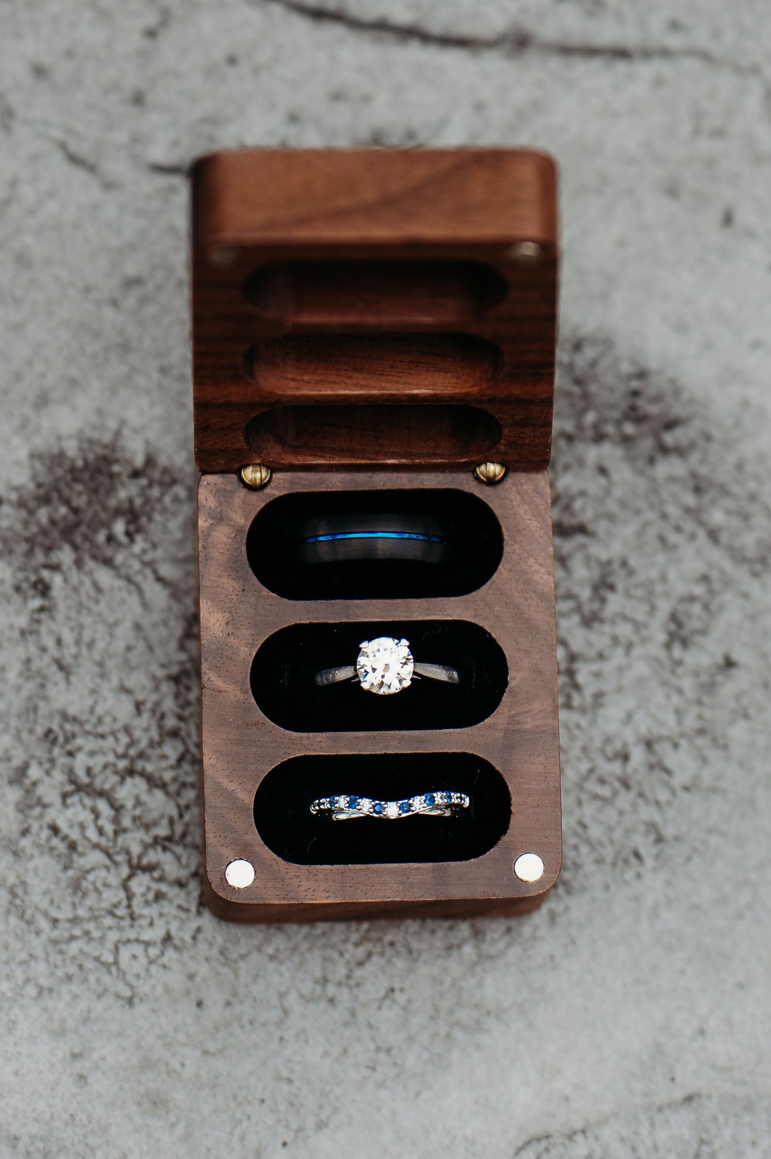 Close-up sequence of wooden ring box opening to reveal diamond engagement ring and matching blue-accented wedding band.
