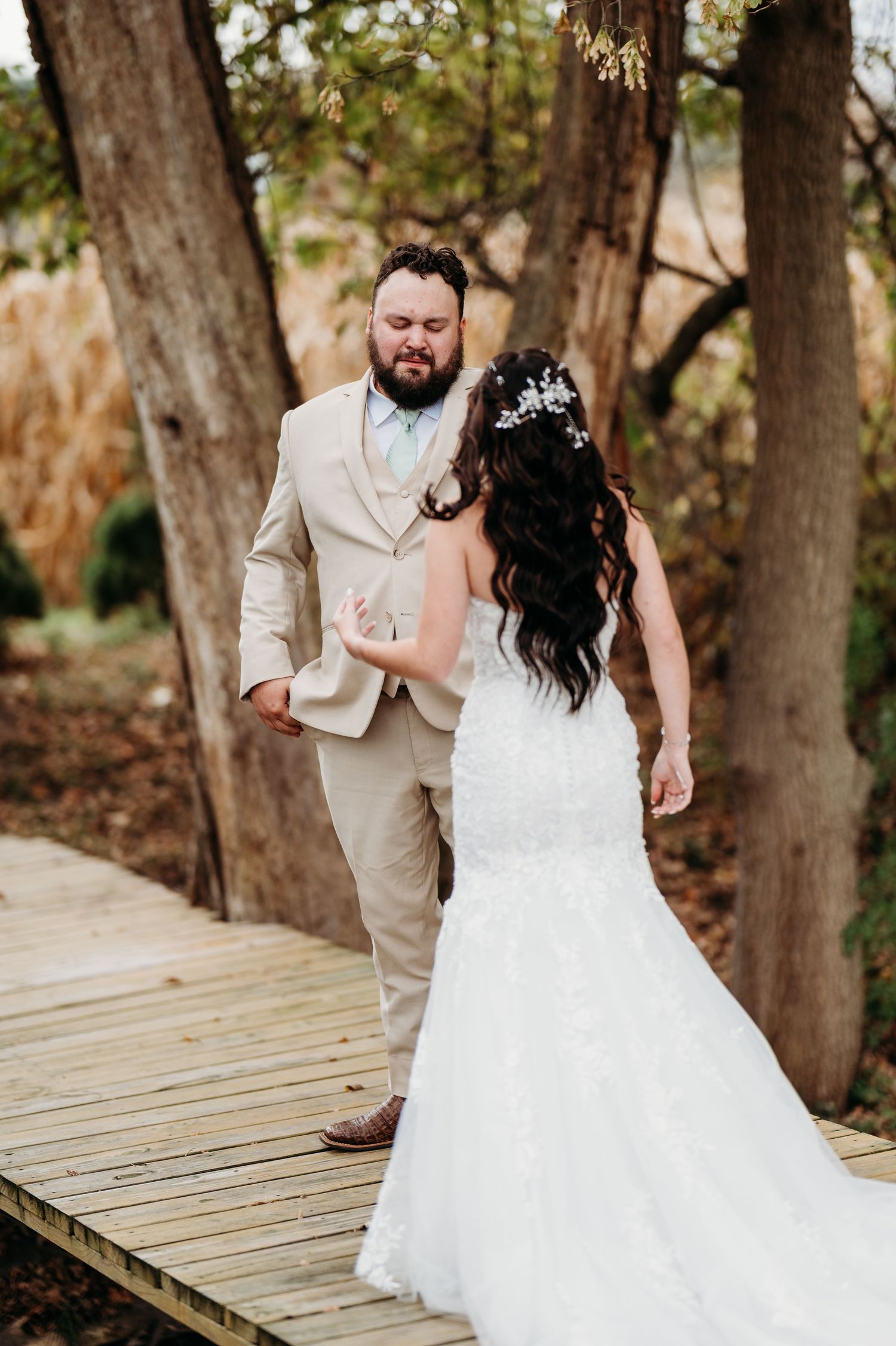 A romantic wedding couple shares playful moments on a wooden boardwalk surrounded by trees.