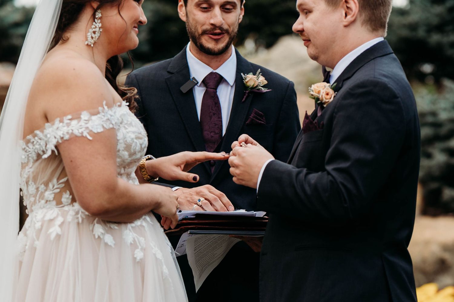 A couple exchanges rings during an intimate outdoor wedding ceremony as loved ones look on.