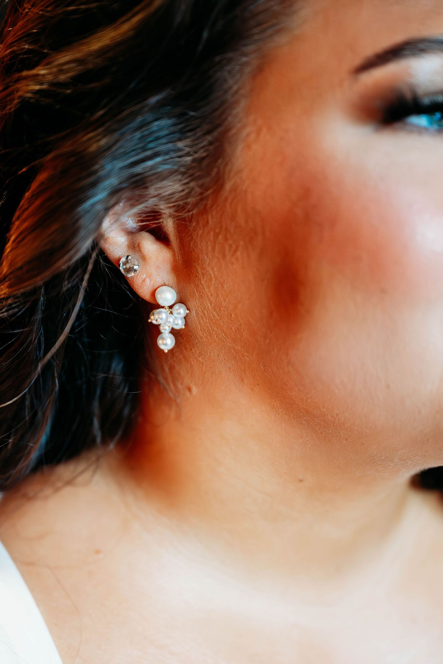 Close-up of a bride wearing elegant pearl and crystal cluster earrings with a small stud on her upper ear.