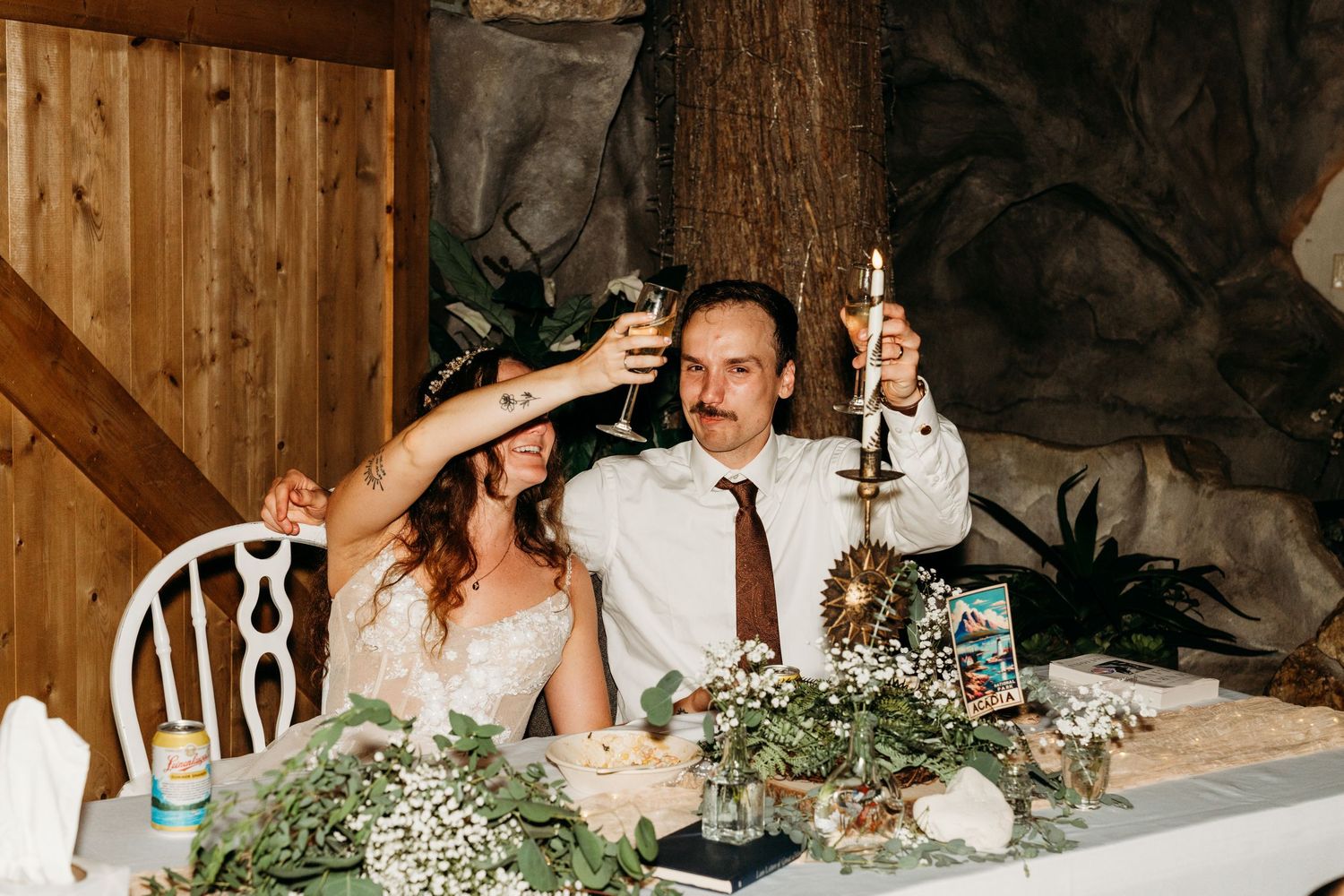 Bride and groom raising champagne glasses in a toast at their rustic wedding reception table adorned with white floral arrangements.