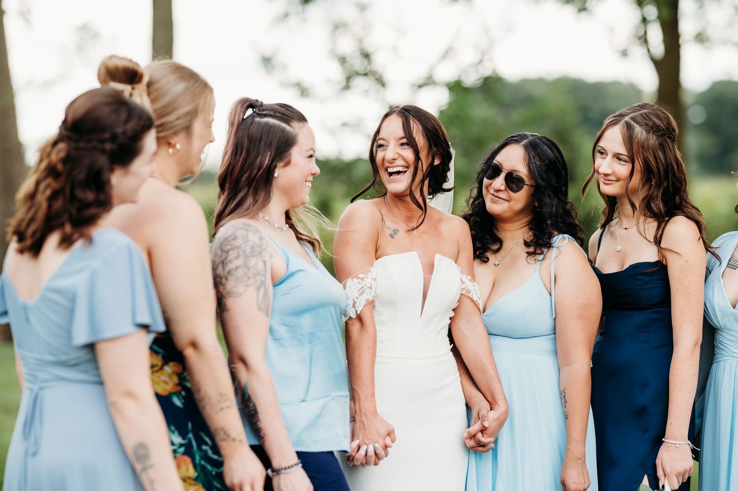 Bridesmaids in light blue dresses and navy blue dresses stand together outdoors for wedding party photos.