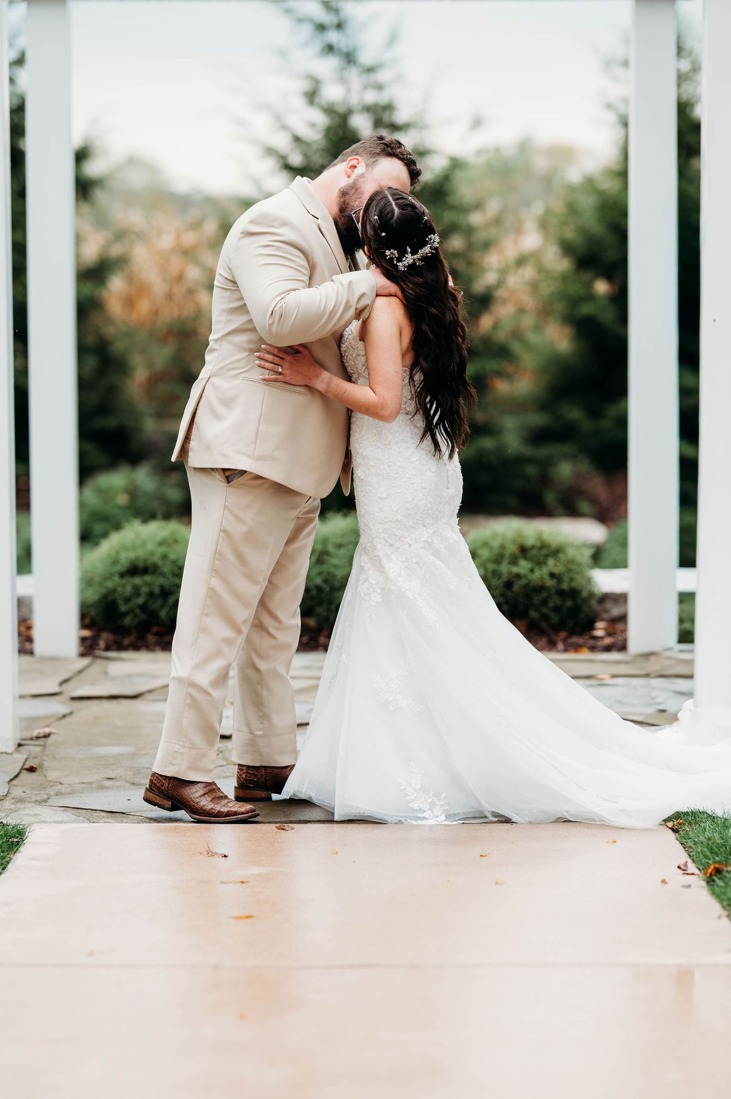 A tender moment between newlyweds sharing their first kiss under a white pergola.