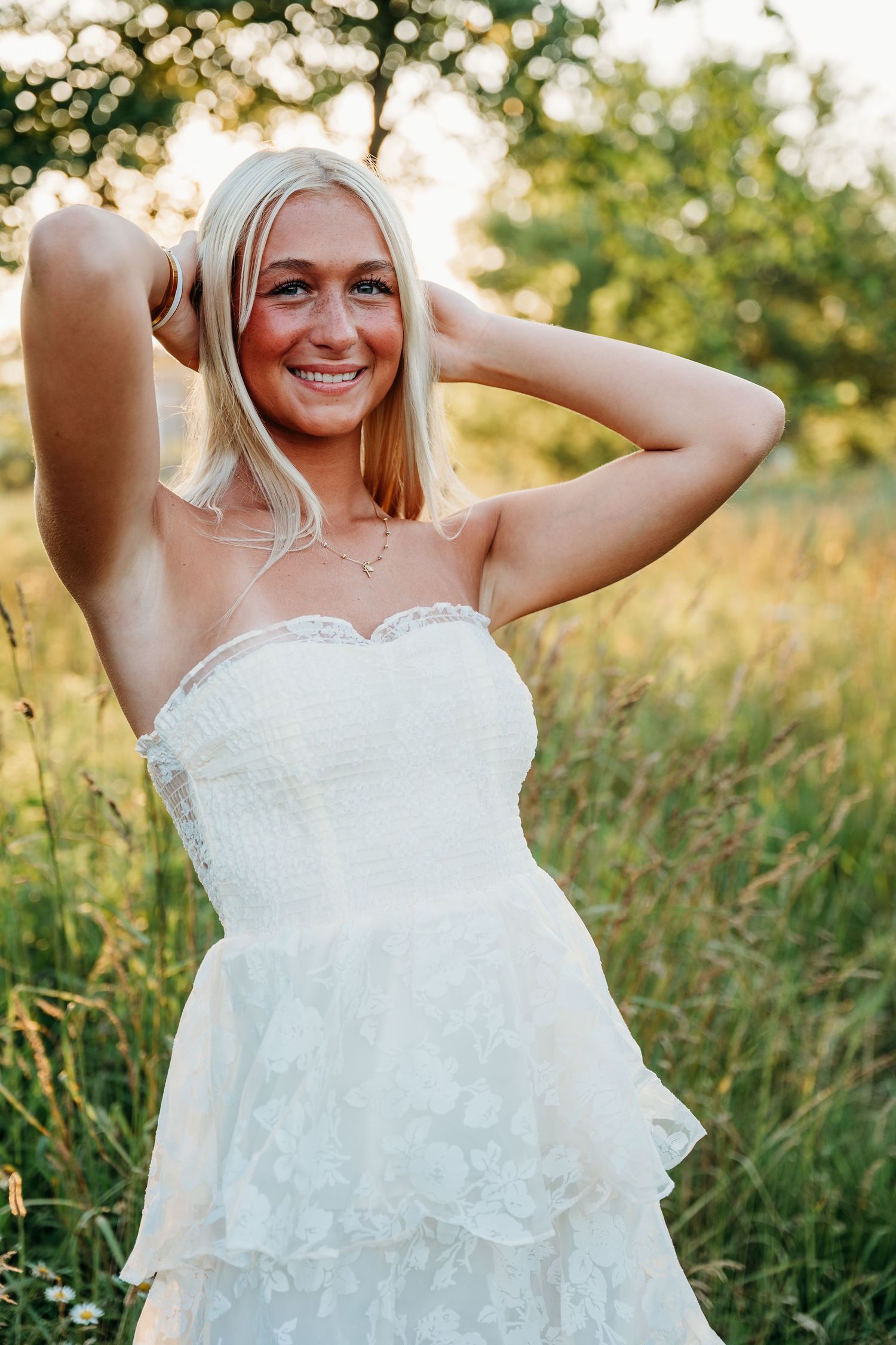 Delicate layers of white lace and ruffles cascade down a strapless wedding gown in a summer field.