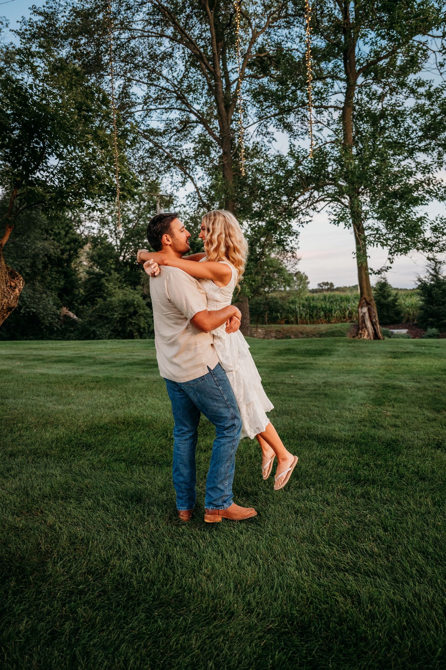 A couple dances playfully on a lush green lawn at sunset with trees in the background.