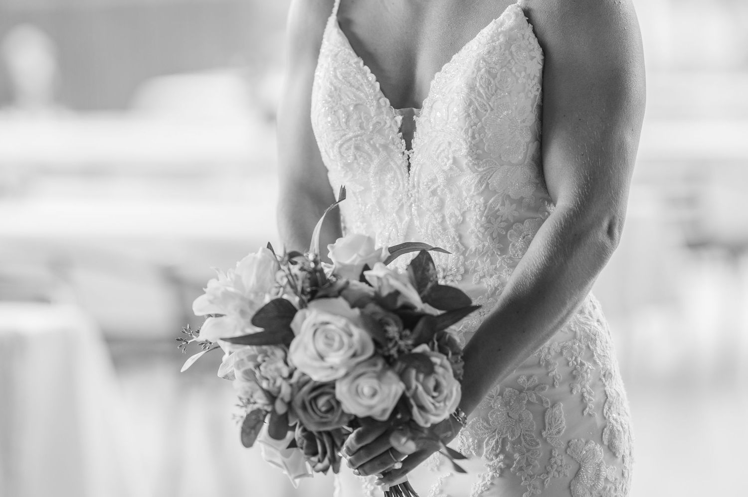 Black and white photo of a bride in lace gown holding a bouquet of roses and greenery on her wedding day.