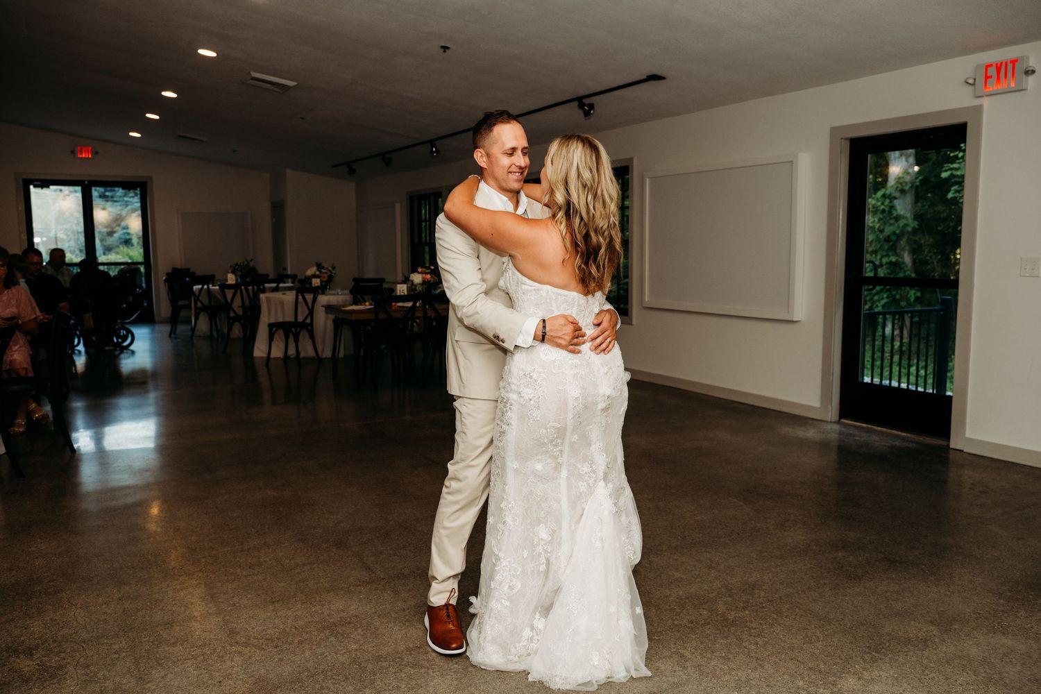 A couple shares their first dance in an elegant white reception hall with polished concrete floors.
