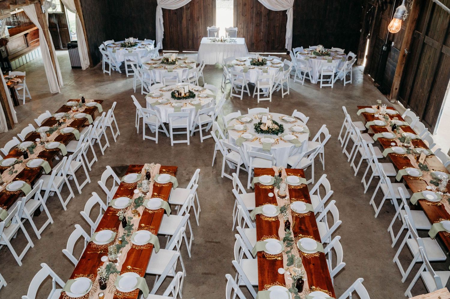 Wedding reception venue setup with white folding chairs and orange table linens in a rustic indoor space.