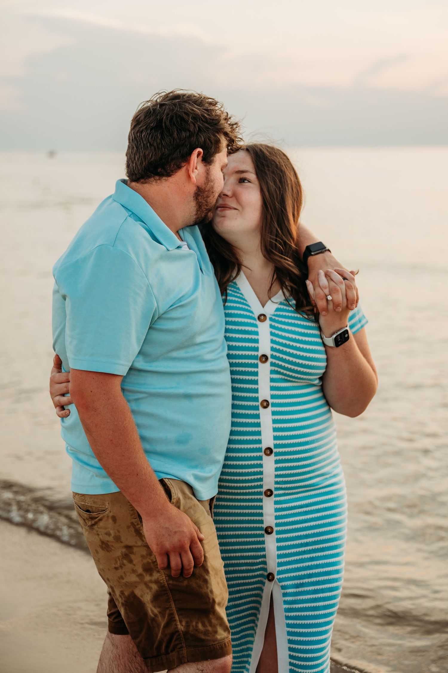 A couple wearing matching turquoise outfits share a romantic moment at sunset by the ocean.