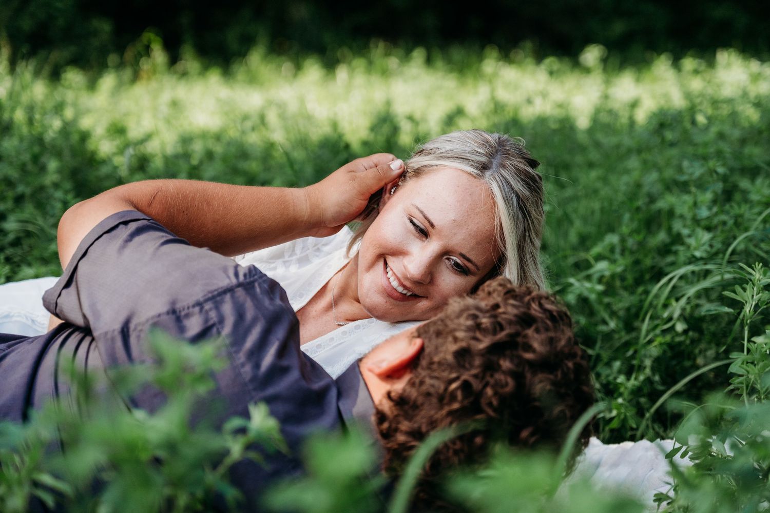 People lying in lush green grass with purple wildflowers on a sunny summer day enjoying nature.