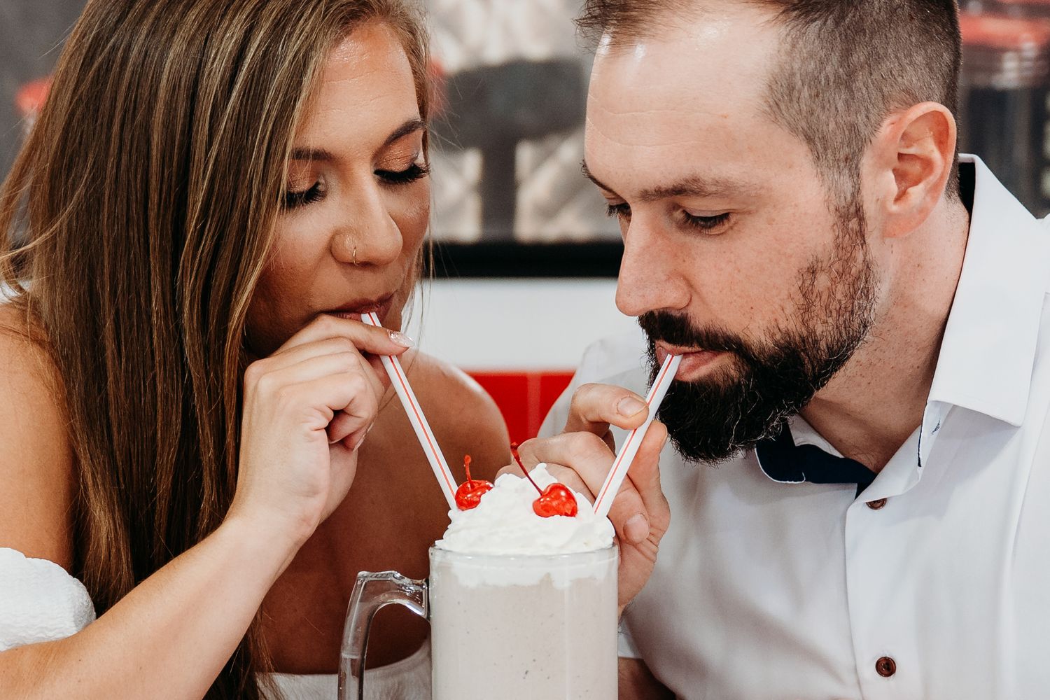 Couple sharing a milkshake with whipped cream and cherry through straws at a restaurant.