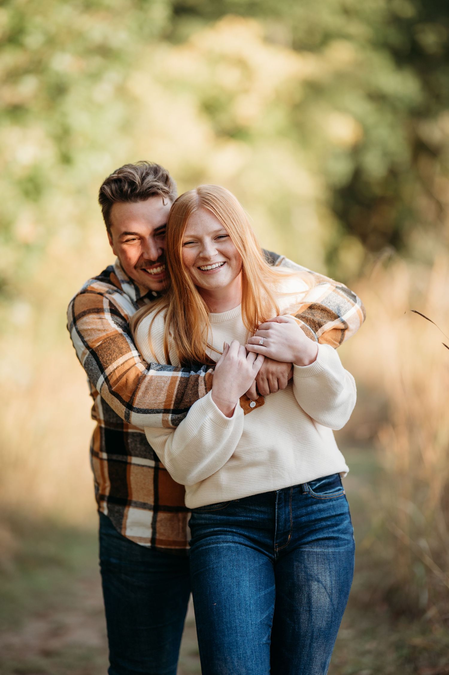 A couple laughs together while sharing a warm moment outdoors wearing casual fall attire.