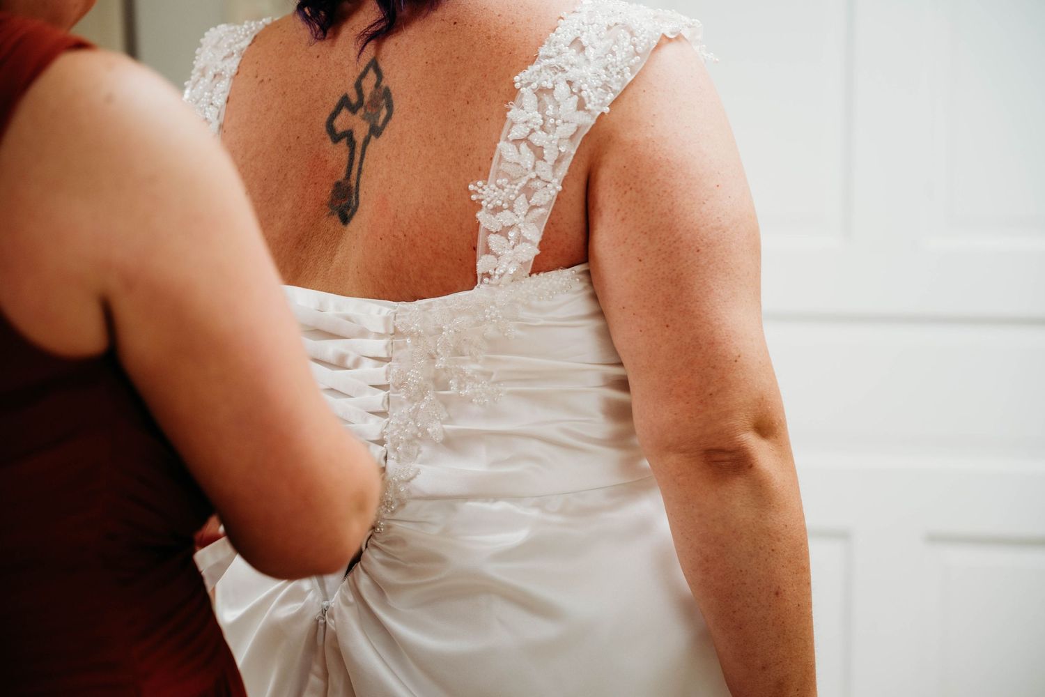 Delicate white lace detailing on the back of a wedding dress with a tattoo visible on the wearer's shoulder.