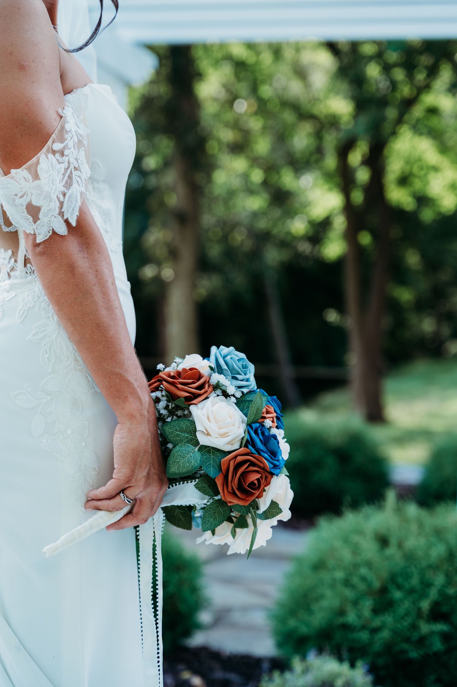 Close-up of bride holding a rustic bouquet with blue and white flowers against her white lace dress.