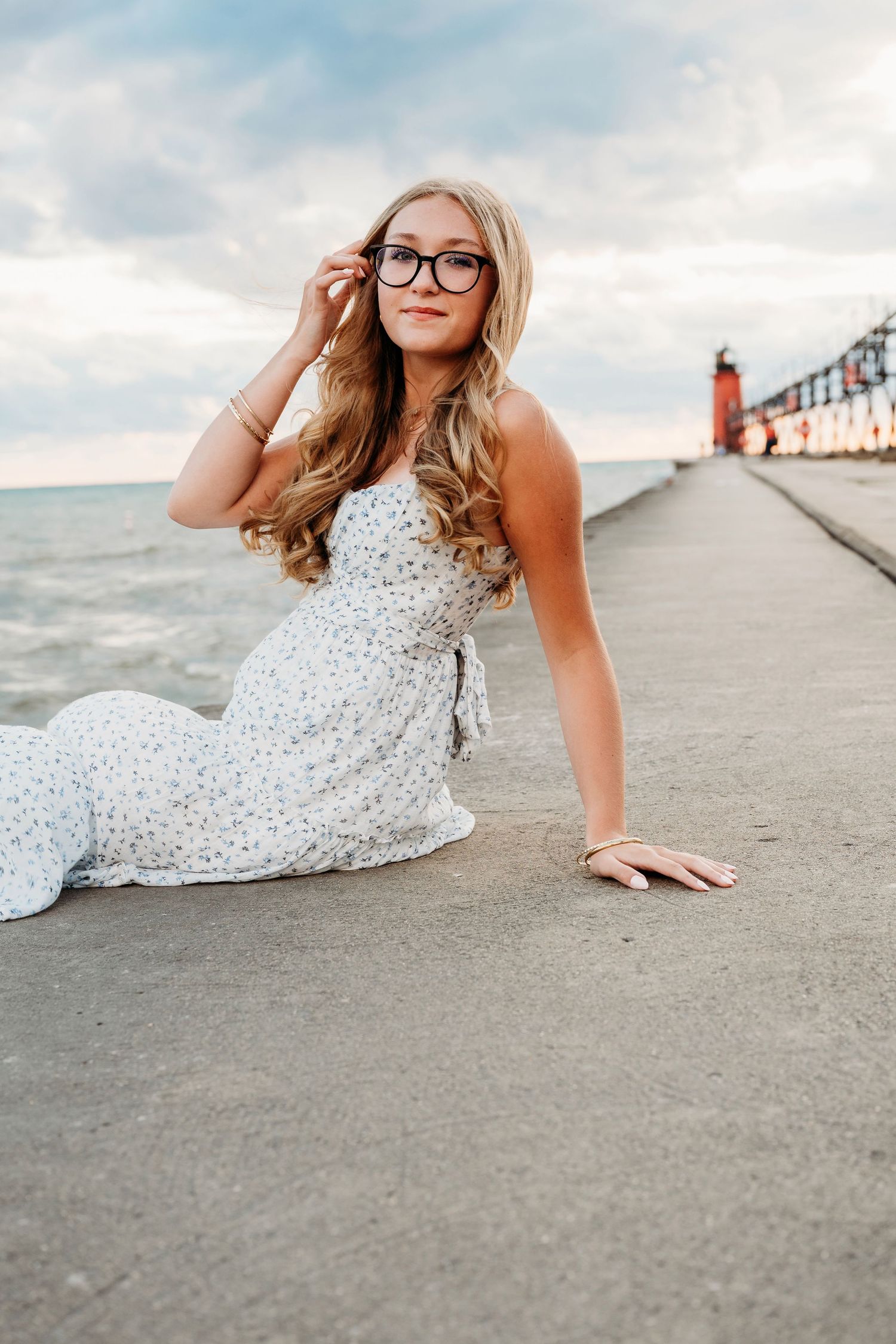 Person in flowy white dress reclining on concrete pier with lighthouse in background.