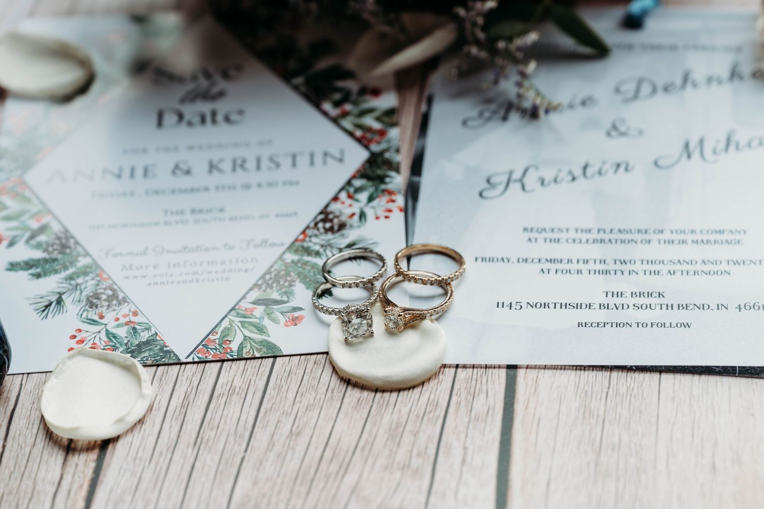 Wedding rings and elegant invitation cards displayed with delicate floral details and calligraphy on a light surface.