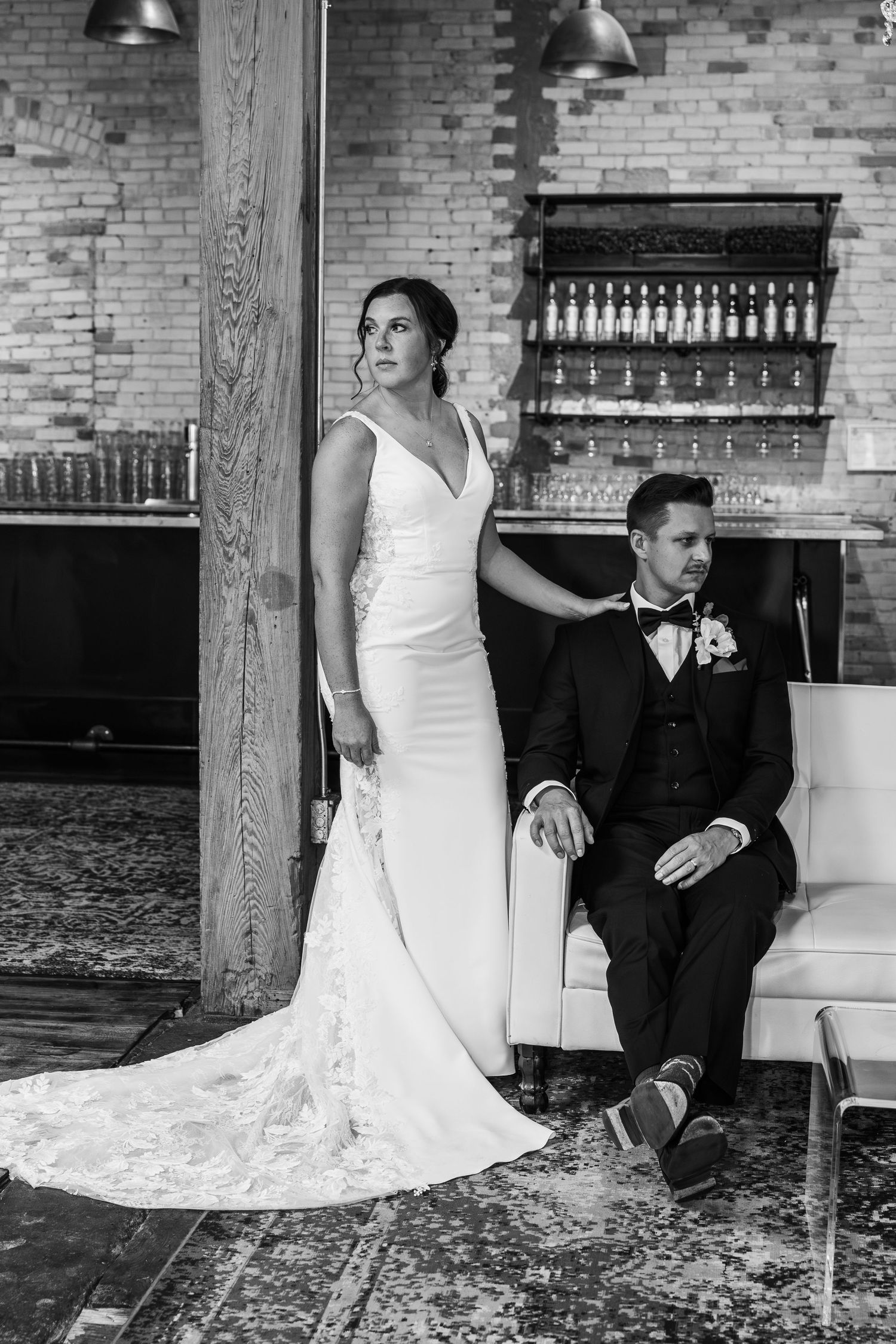 Black and white wedding portrait series showing couple sitting on white couch against exposed brick wall.