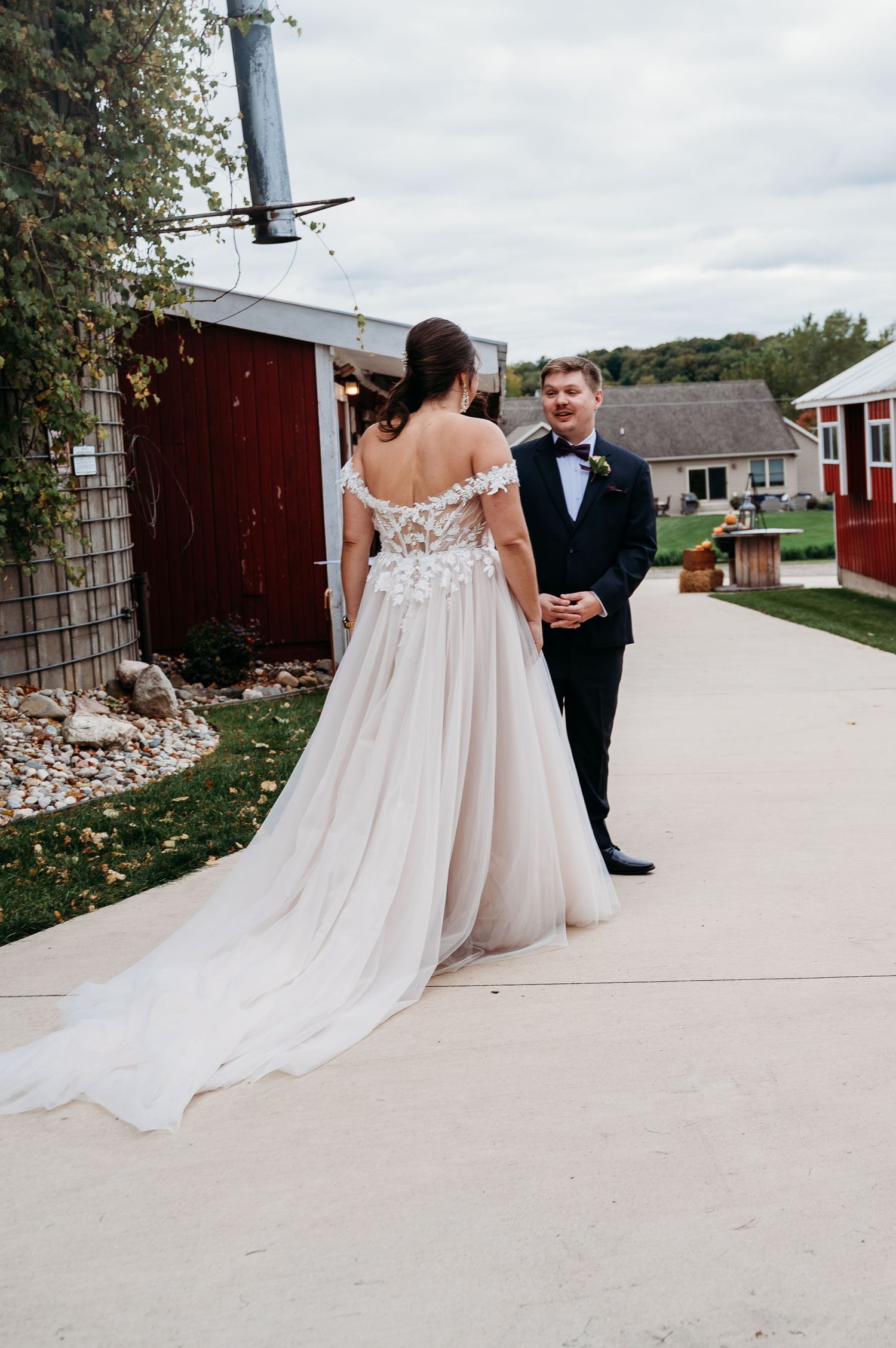 A couple in wedding attire walks down a concrete path with a red barn visible in the background.