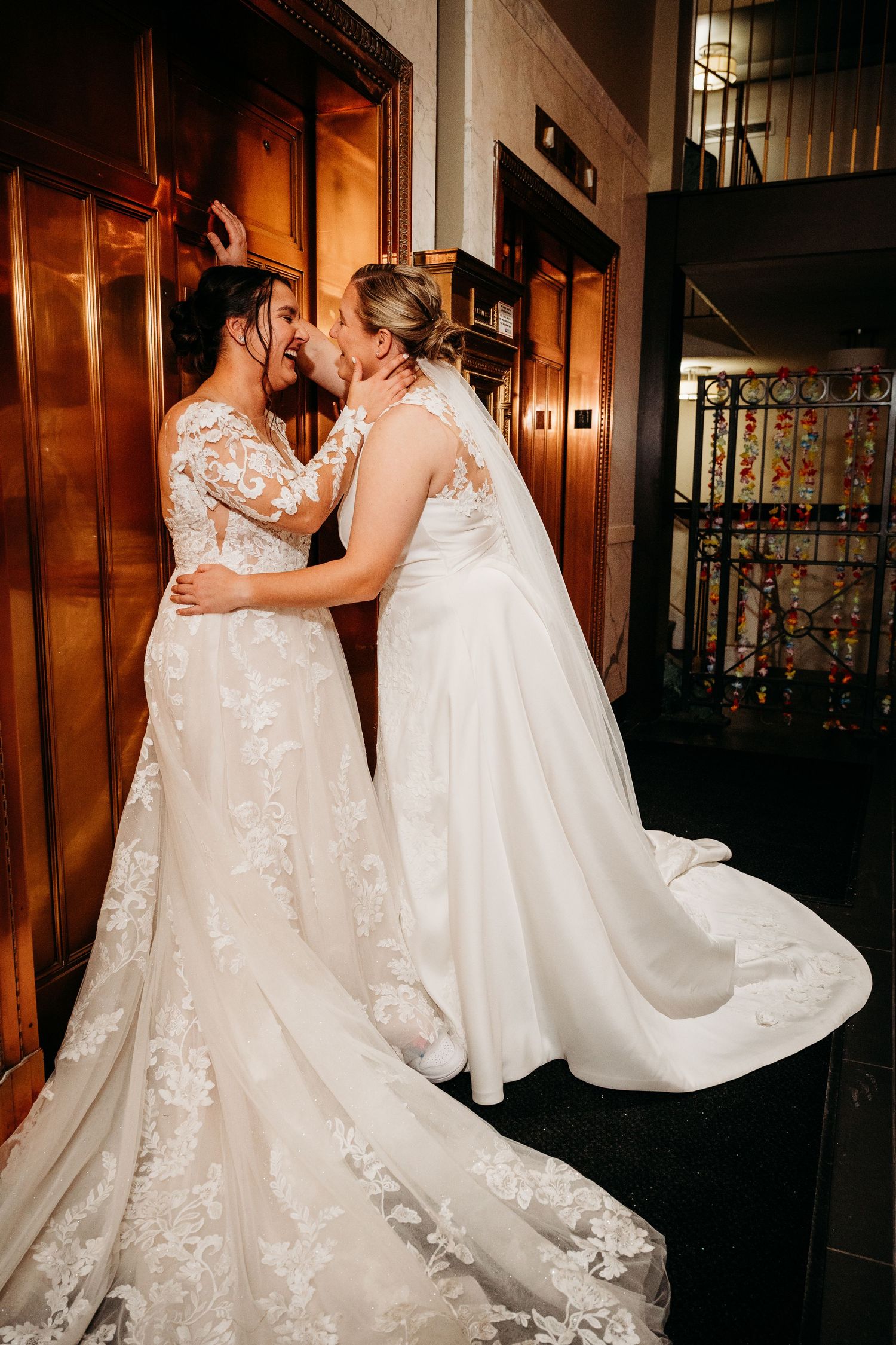 Two people in elegant white wedding dresses dance together in a warmly lit indoor venue.