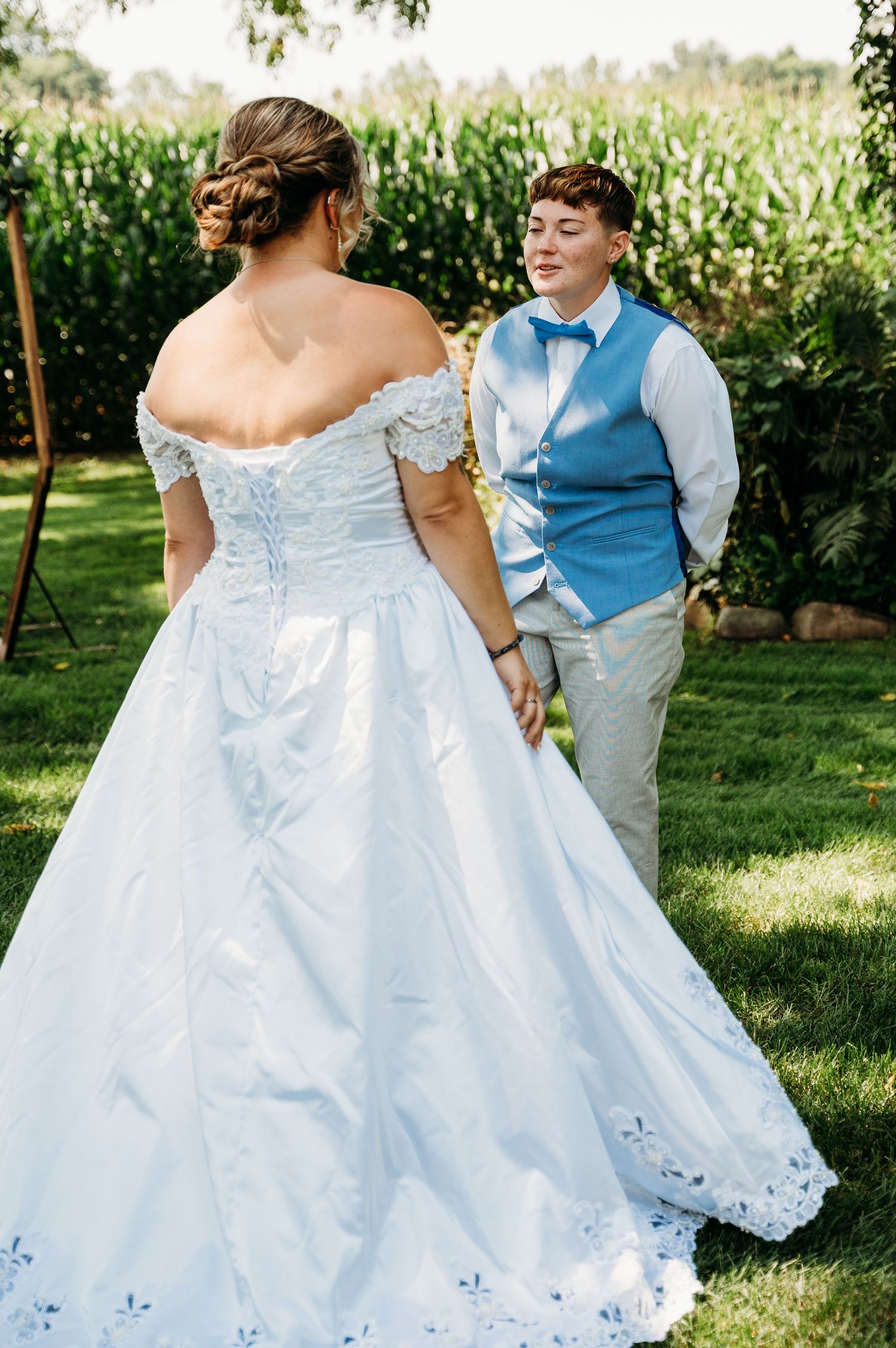 Wedding couple in garden setting with bride wearing white off-shoulder gown and partner in light blue vest.