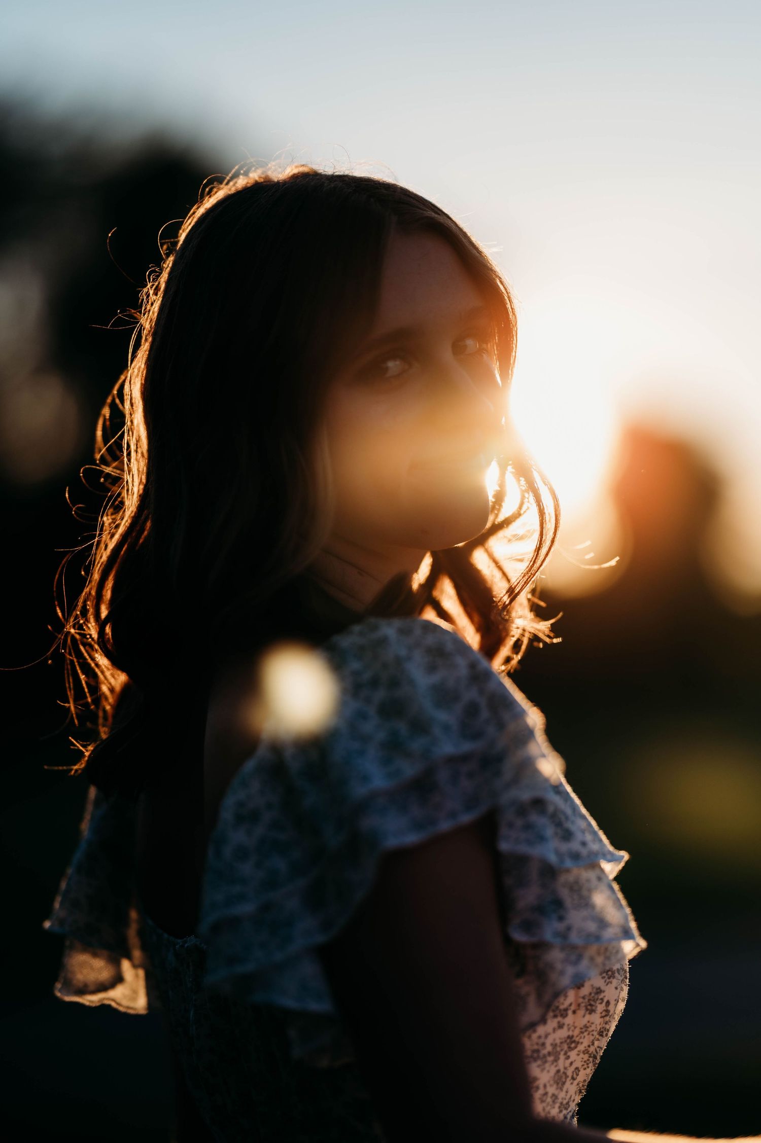 Close-up portrait of brunette woman in floral dress with stunning golden hour sun flare bokeh.