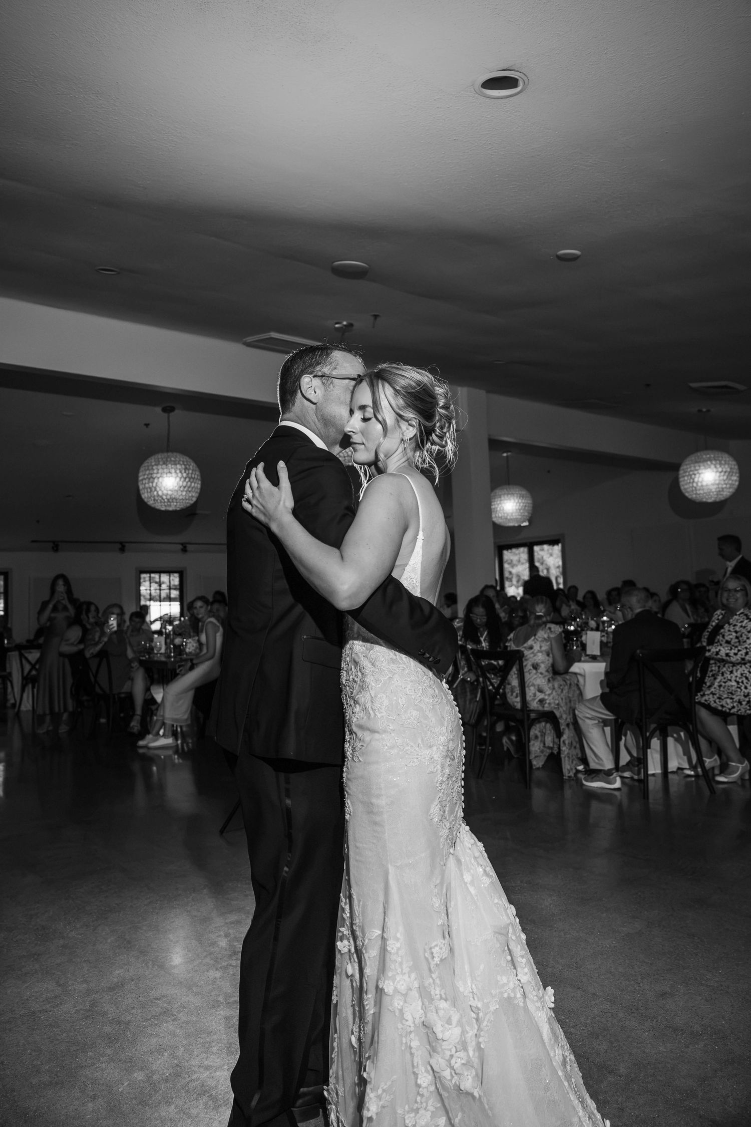 Black and white photo of a bride and groom sharing their first dance at a wedding reception.