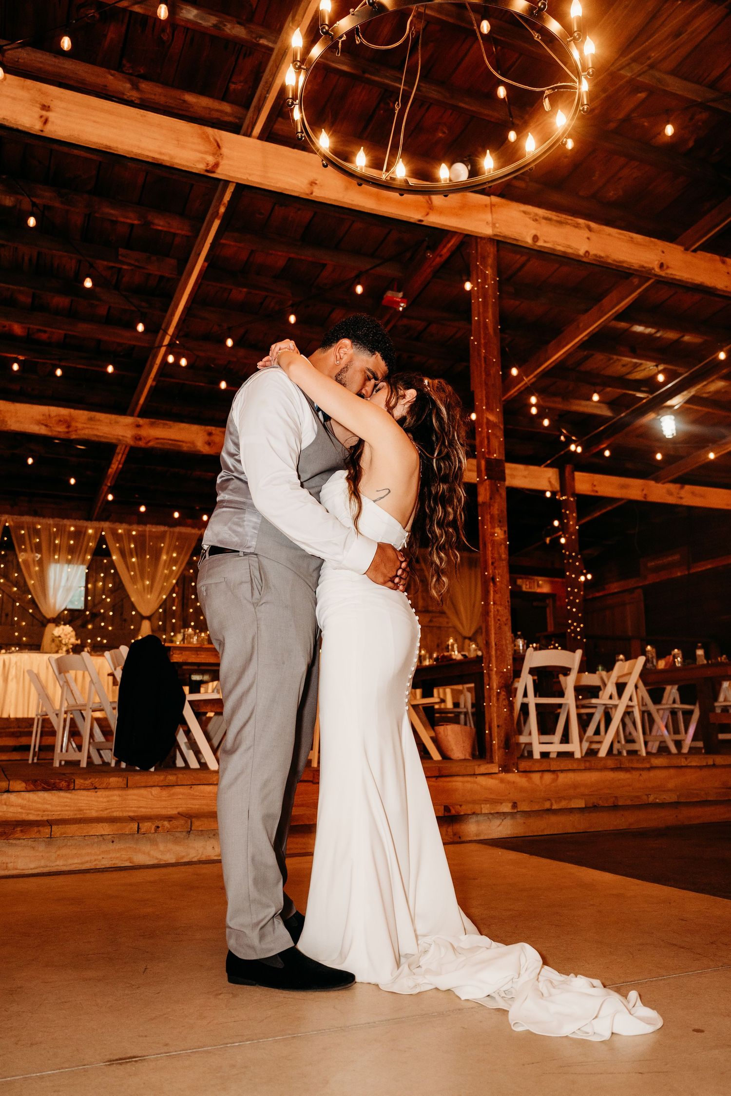 A romantic first dance sequence at a rustic barn wedding reception illuminated by warm string lights.