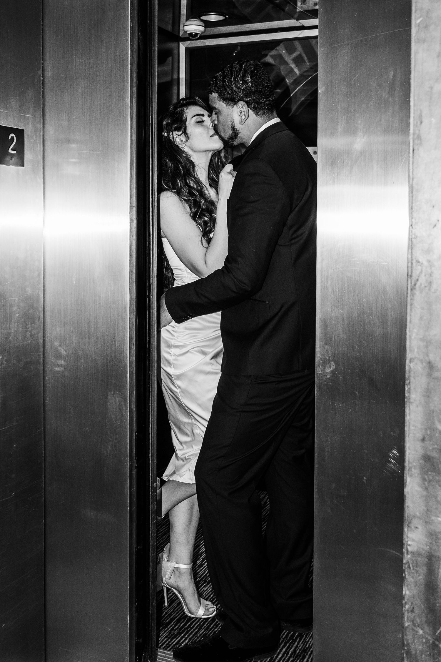 A romantic black and white photograph of a couple sharing an intimate moment in an elevator doorway.