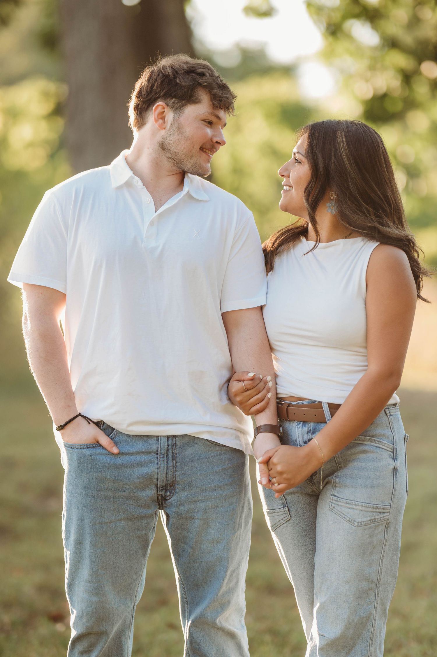 Couple in white tops and denim share loving glances during an outdoor summer photoshoot.
