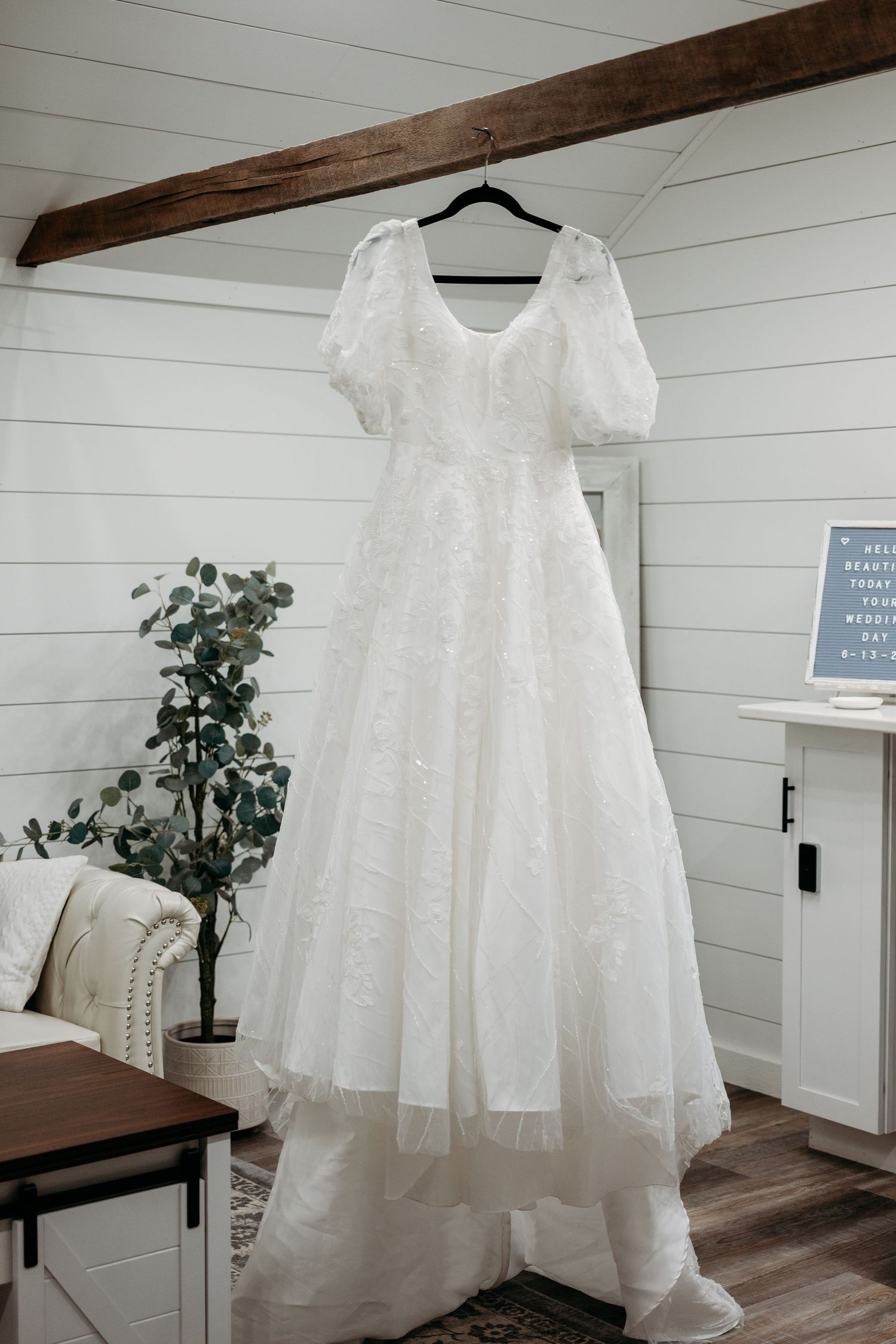 White lace wedding dress with puff sleeves hanging on a hanger in a rustic farmhouse bridal suite.