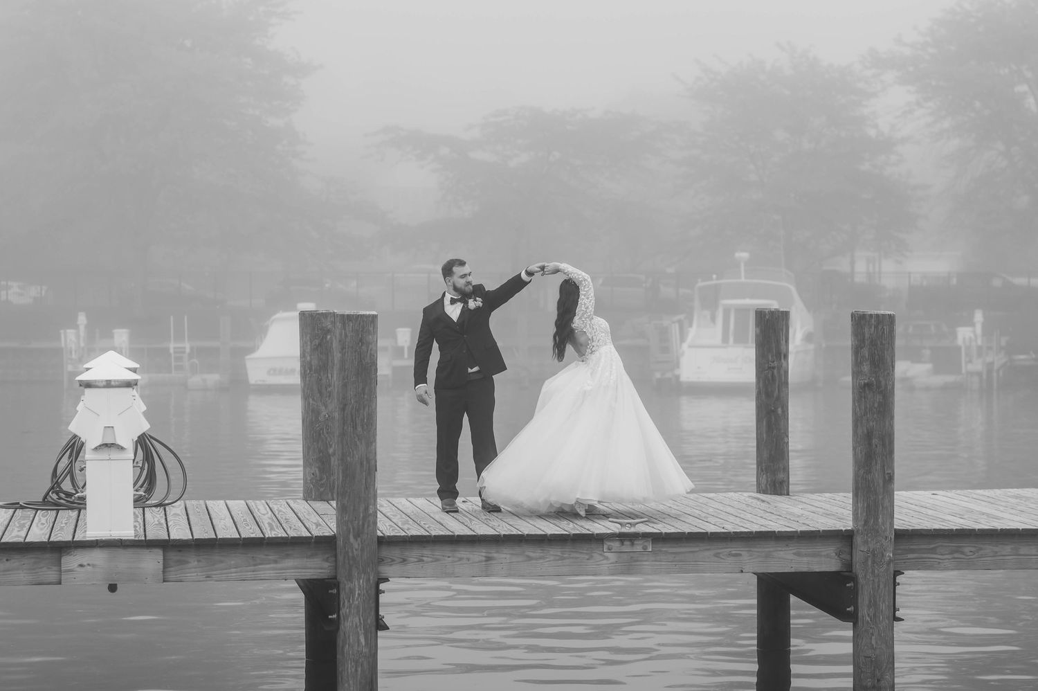 Bride and groom dancing on a foggy waterfront dock in a romantic black and white wedding photo.