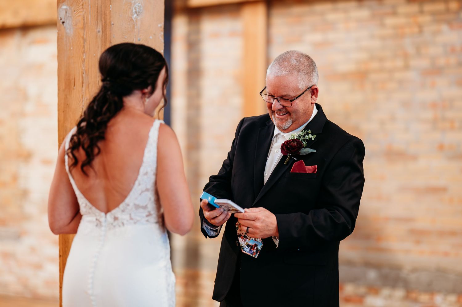Bride and groom sharing an emotional first look moment, reading vows beside a rustic brick wall at their wedding.