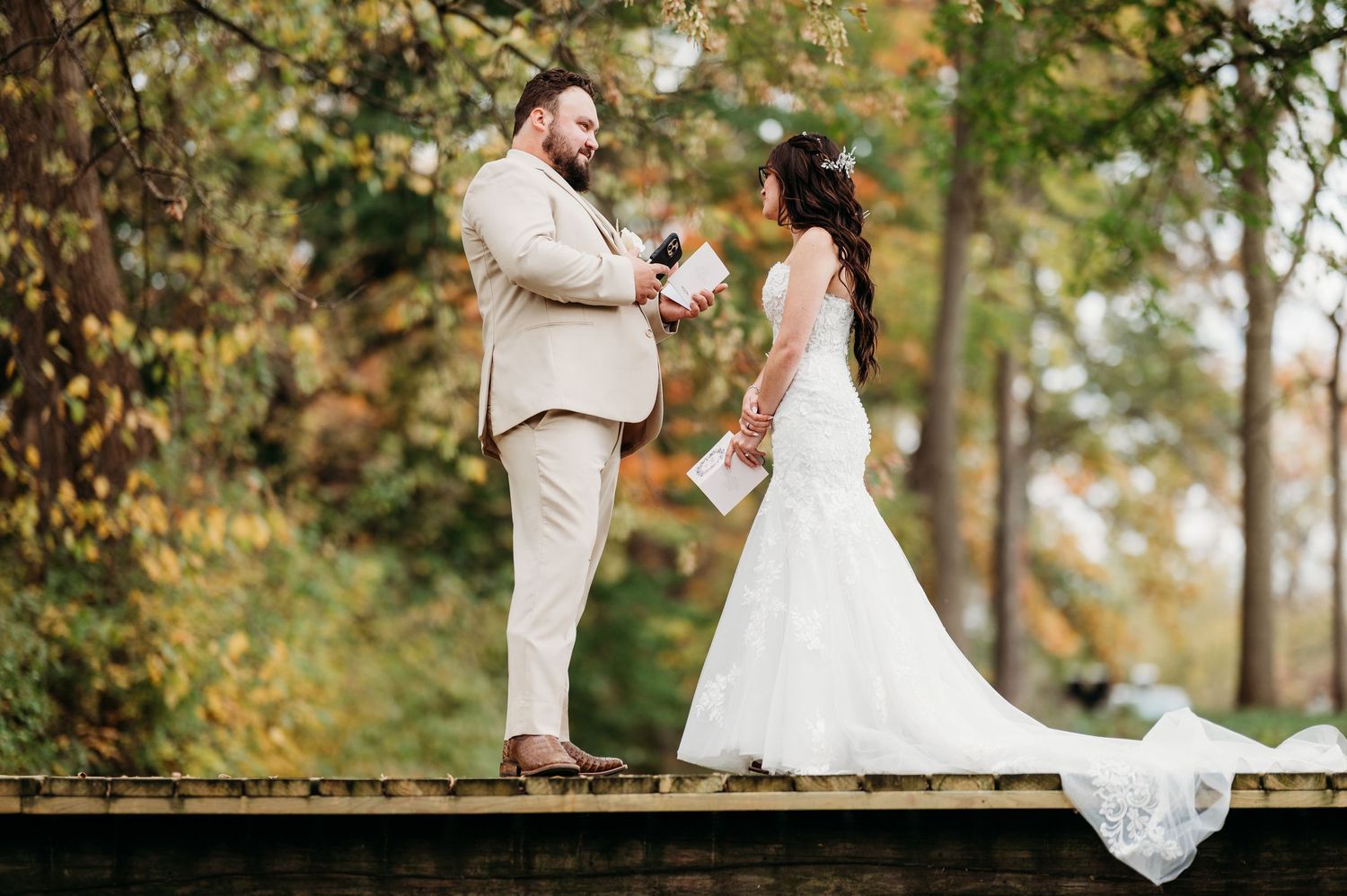 Bride and groom exchange vows outdoors on a wooden deck surrounded by autumn foliage in a romantic wedding ceremony.