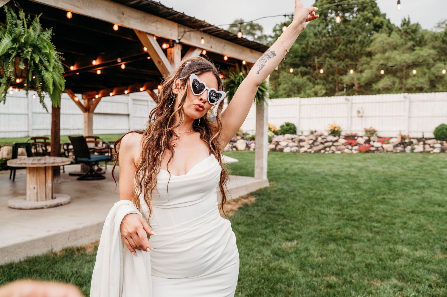 A joyful moment captured at an outdoor wedding reception with string lights and rustic wooden beams overhead.