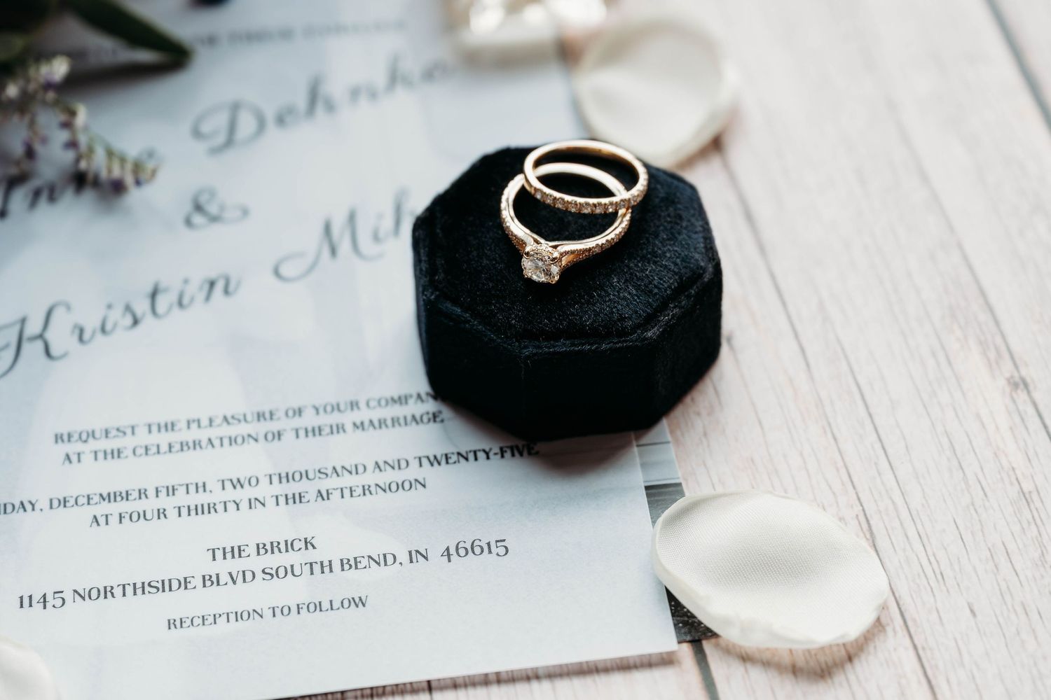 Wedding rings rest on elegant invitation cards with delicate calligraphy text in soft lighting.