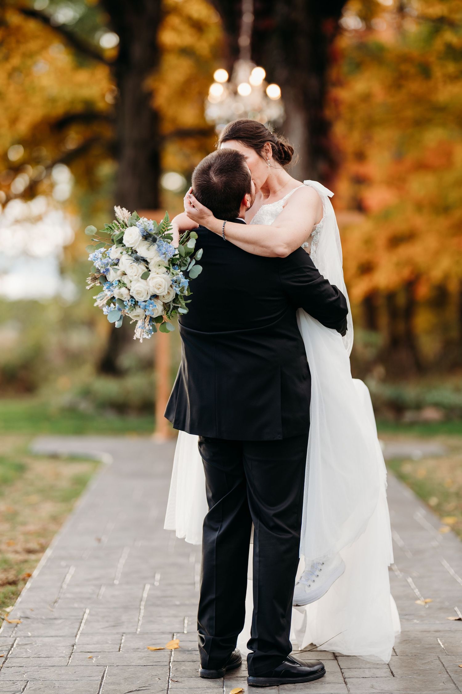 Romantic wedding couple dancing together on a stone path surrounded by autumn foliage and fallen leaves.