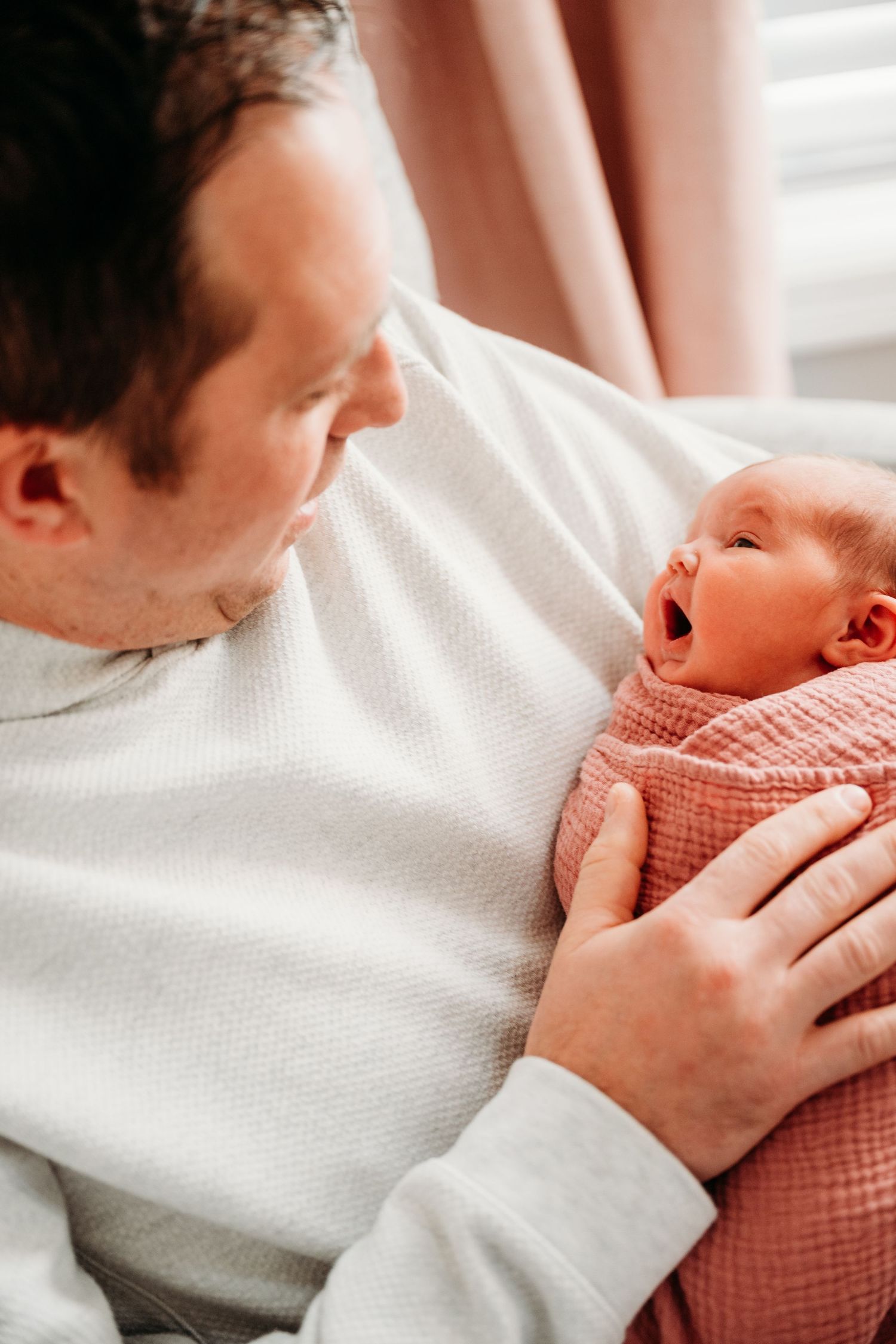 A tender moment between parent and newborn baby wearing a coral-colored outfit while resting on white bedding.