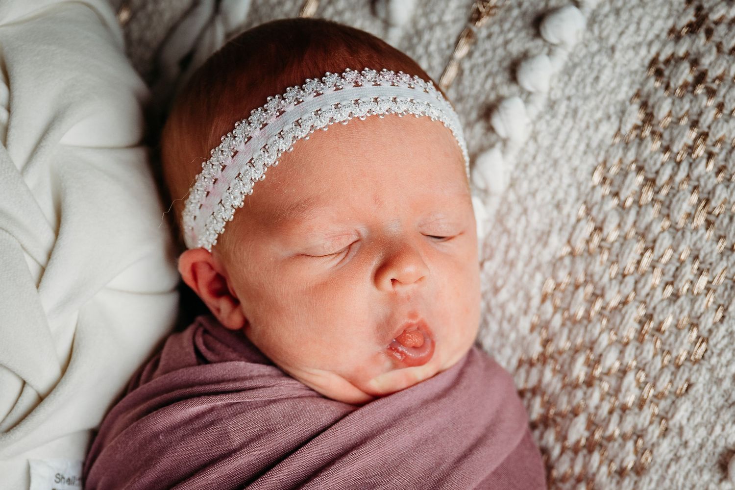 Sleeping newborn in burgundy wrap surrounded by twinkling holiday lights and teddy bears.