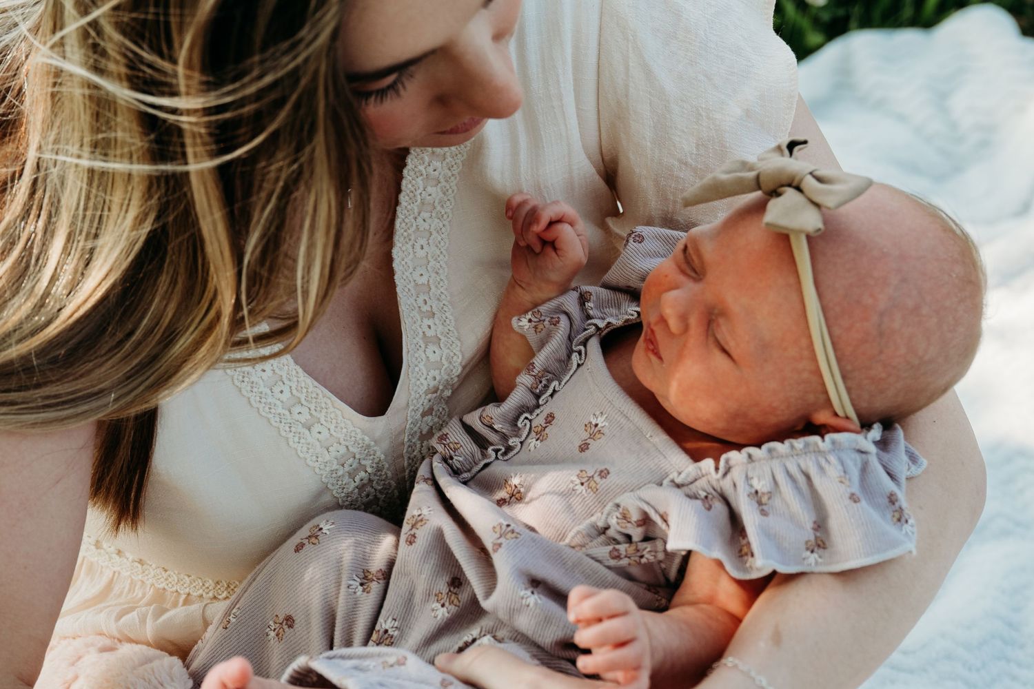 A tender moment between parent and baby wearing a gray dress with bow headband in natural light.