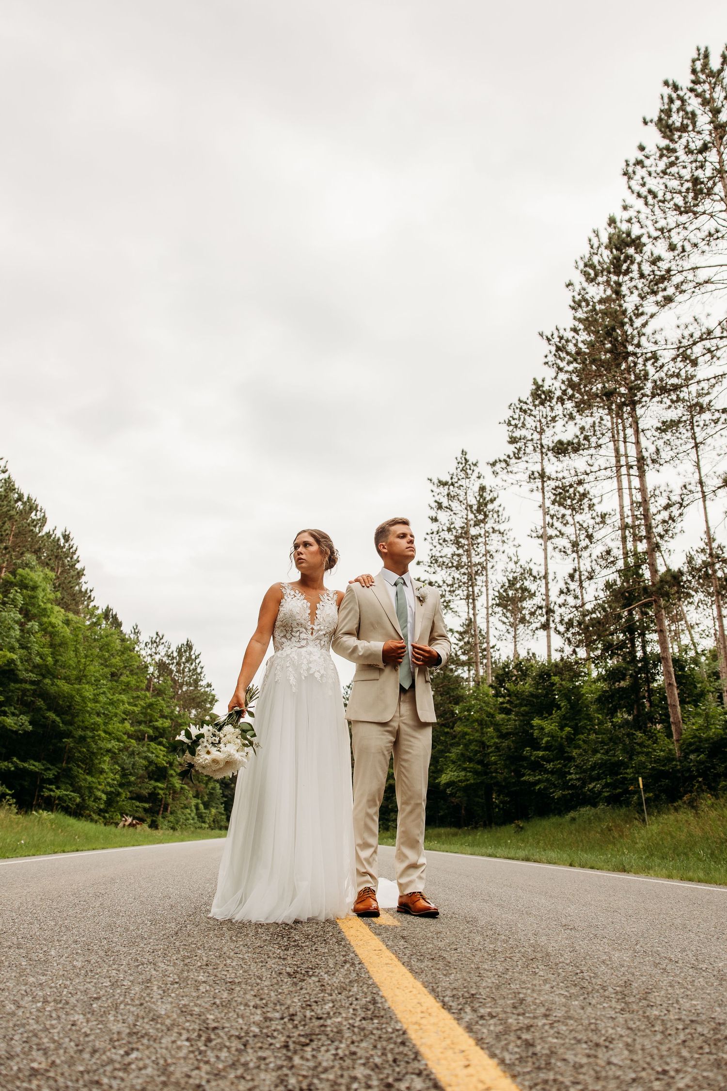 A sequence of artistic wedding photos taken on a rural road with pine trees and yellow lines in the background.