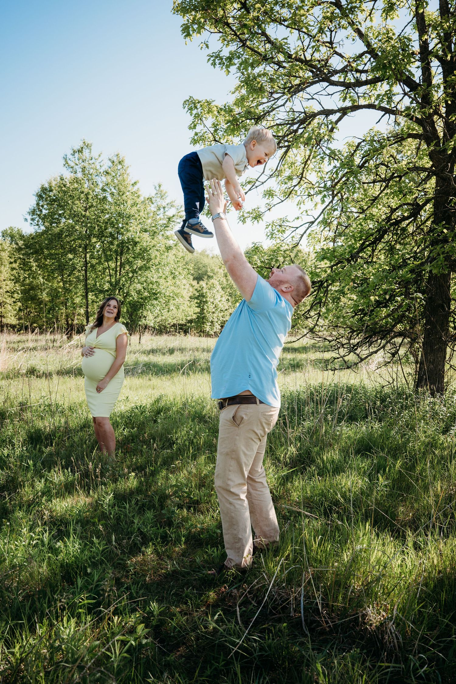 A joyful outdoor family photoshoot in a sunny meadow with green trees and natural lighting.
