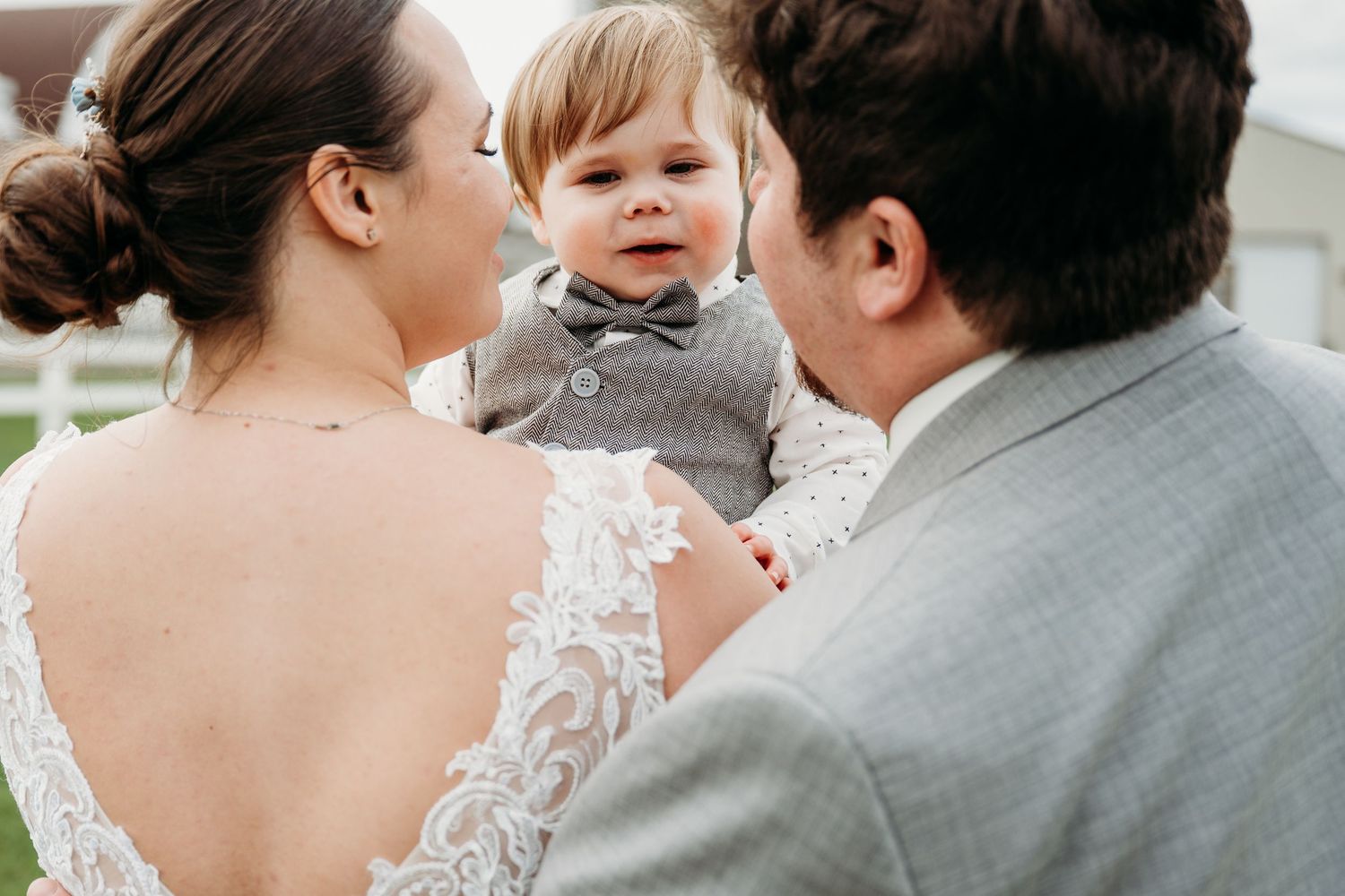 A couple shares an intimate wedding moment as they embrace and kiss while wearing a lace white dress and grey suit.