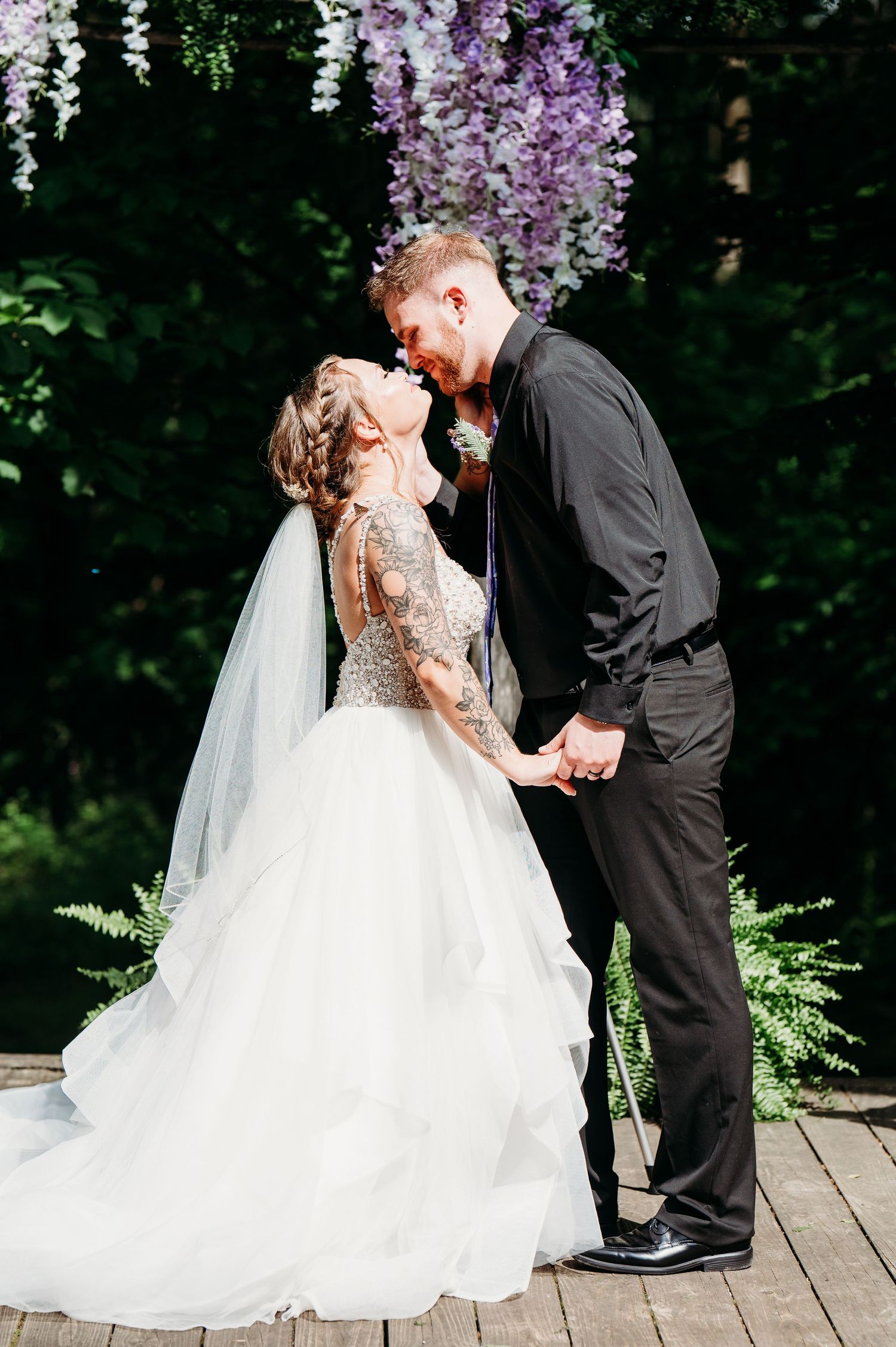 A romantic wedding couple embrace under flowering trees during their outdoor garden ceremony.
