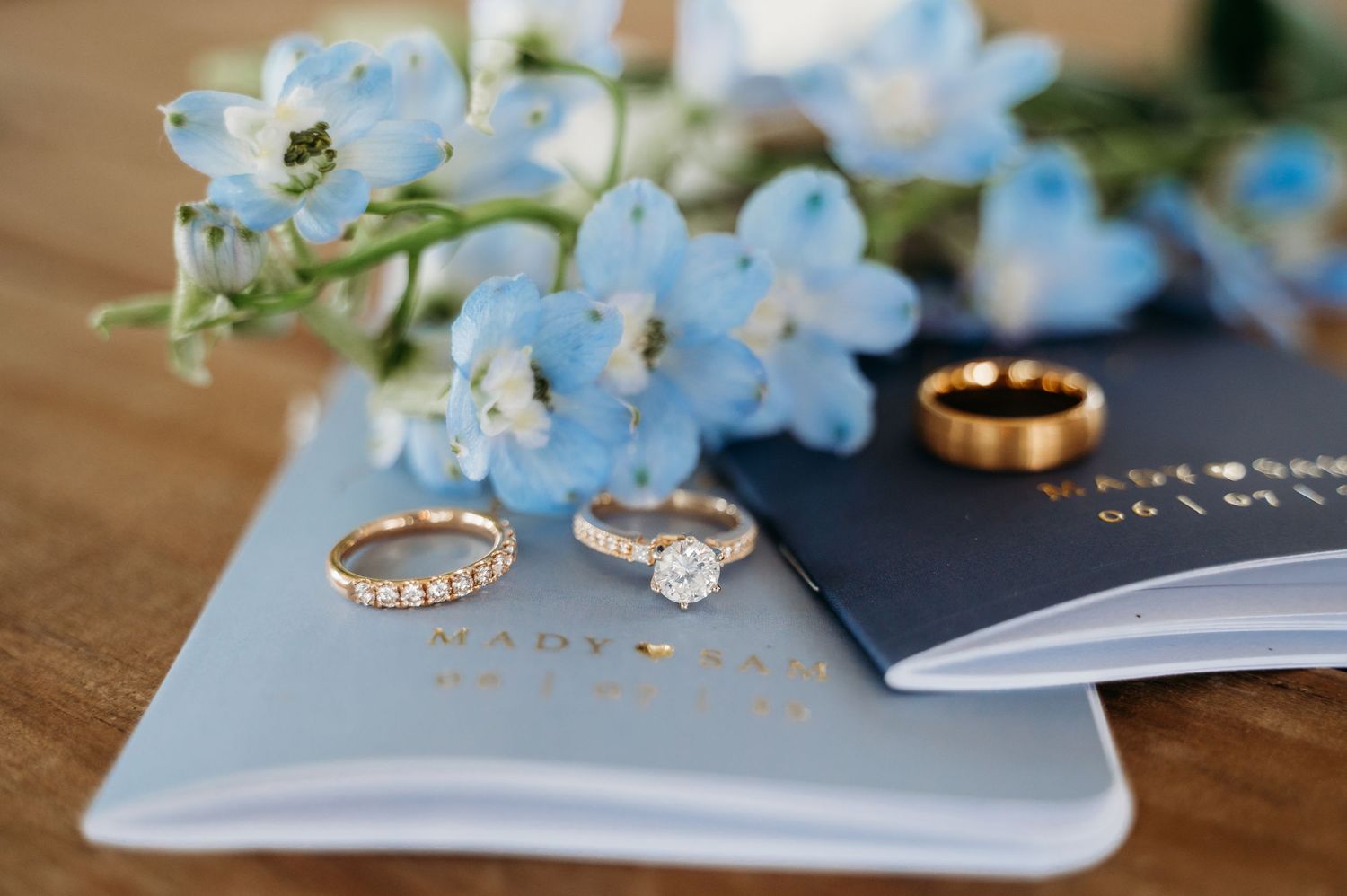 Wedding rings and blue delphinium flowers arranged on a light blue book for a romantic detail shot.