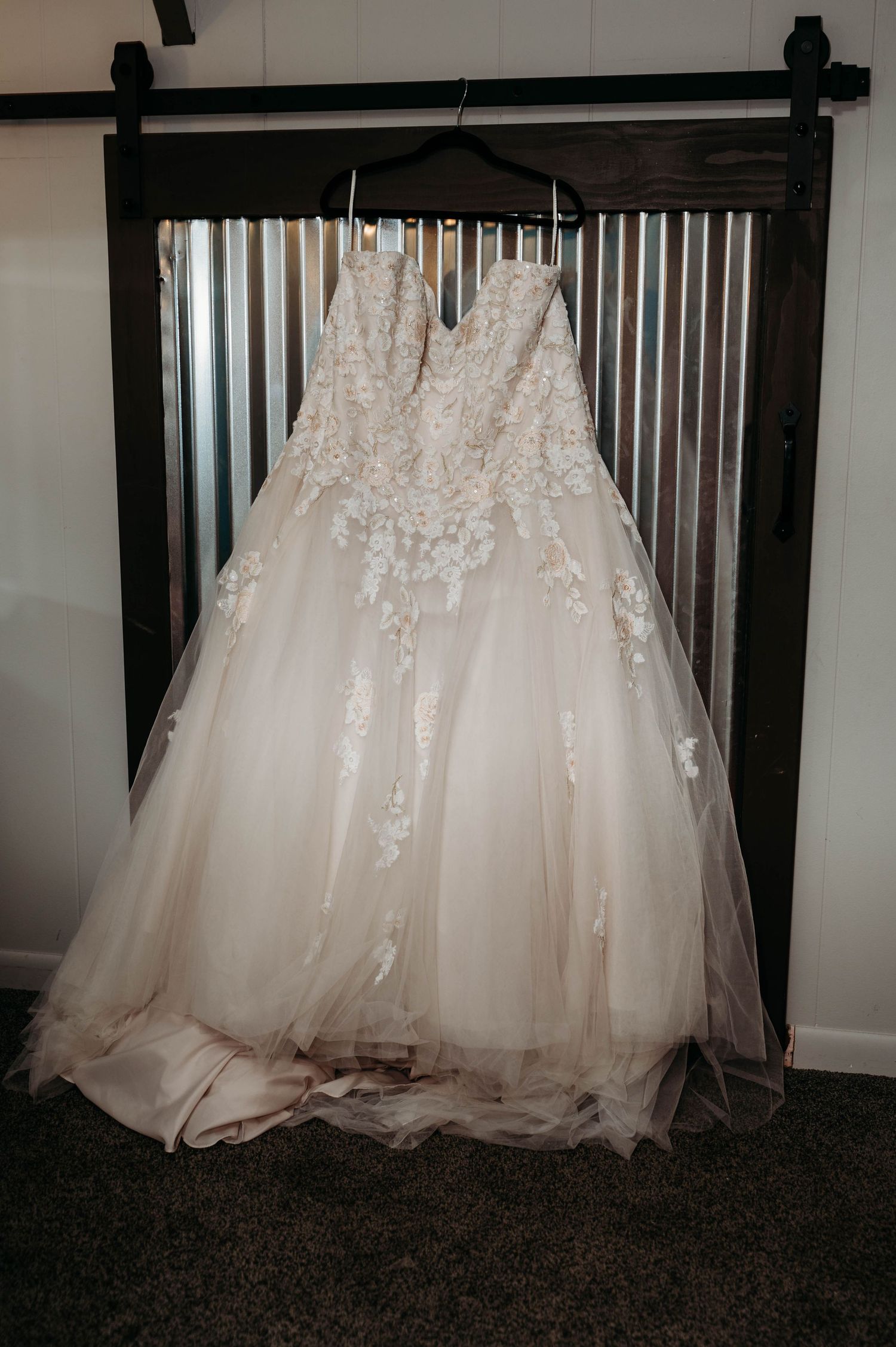 A white wedding dress with delicate lace details hangs elegantly against a dark background.