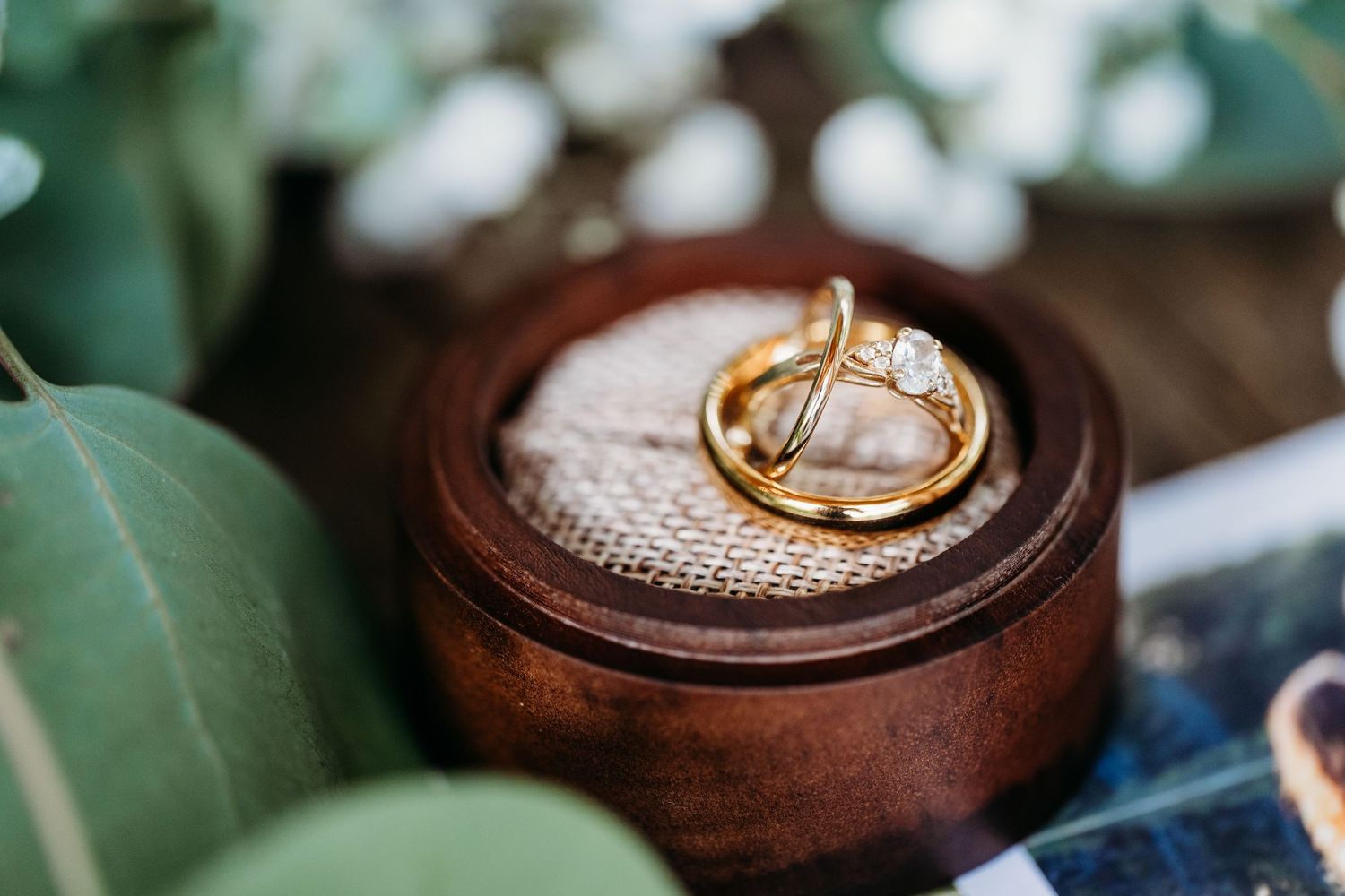 A wooden ring box with a gold wedding band nestled on textured fabric in natural lighting.