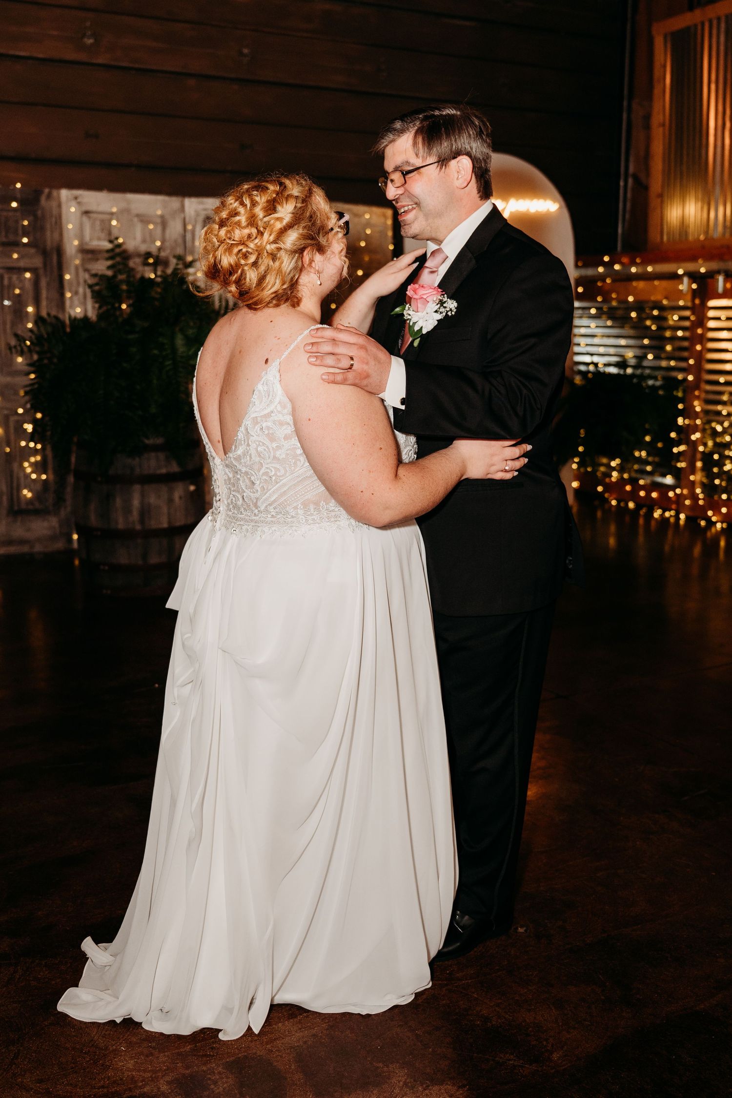 A couple shares their first dance at their wedding reception in a rustic venue decorated with twinkling lights.