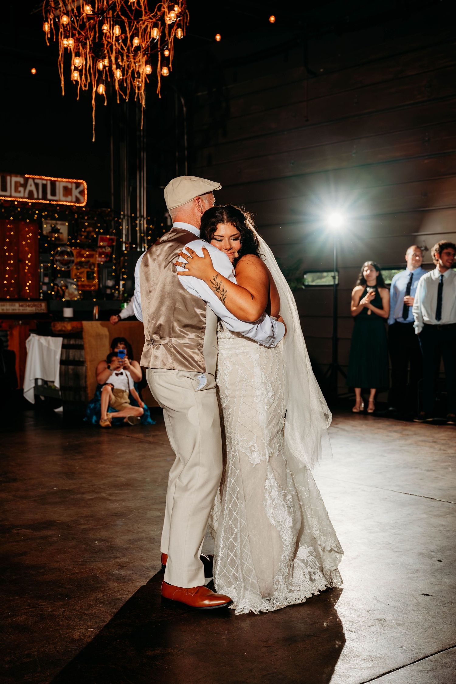 Bride and groom share their first dance under a chandelier at a rustic wedding reception venue.