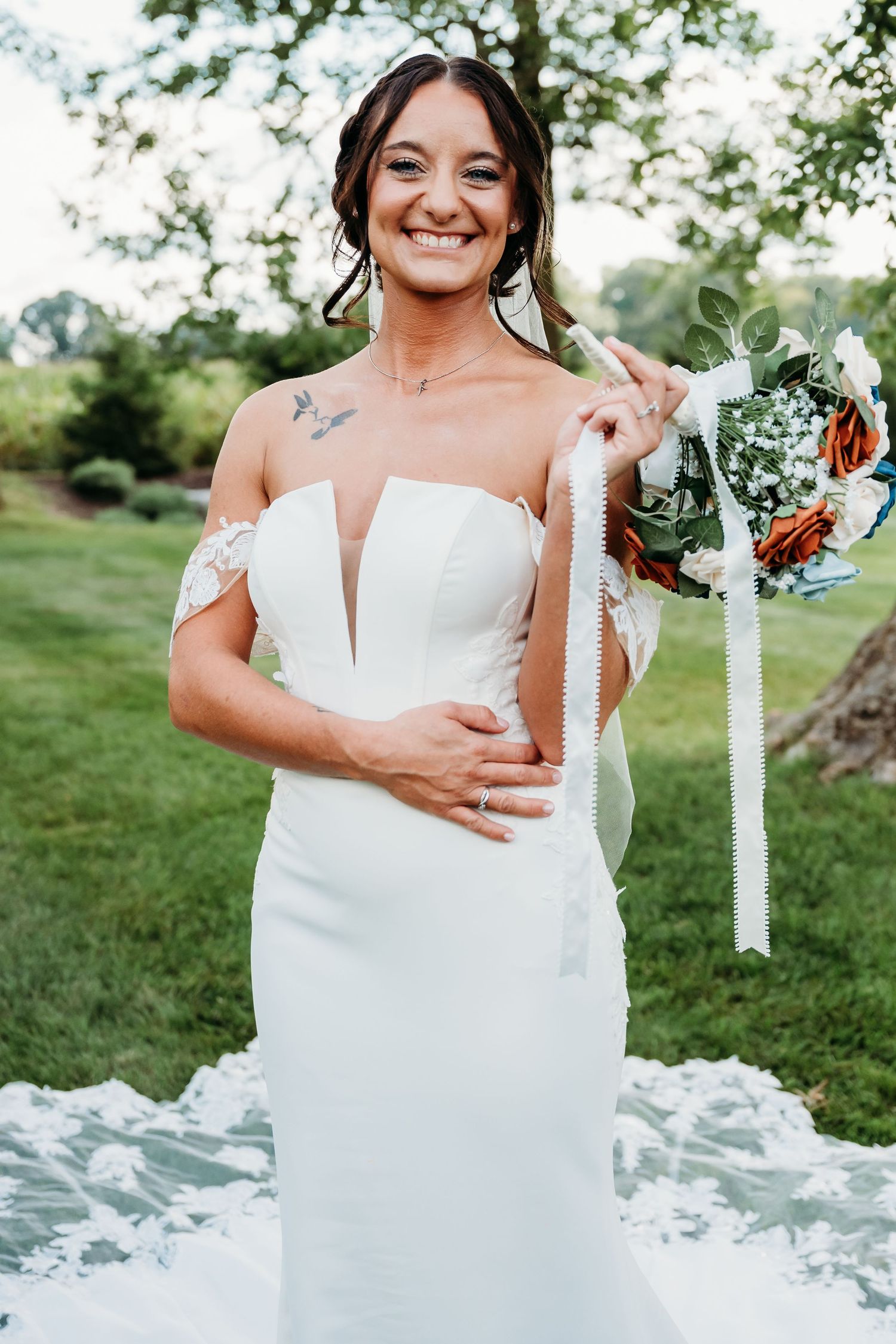 A white off-shoulder wedding dress with a plunging neckline is shown outdoors on a grassy lawn.